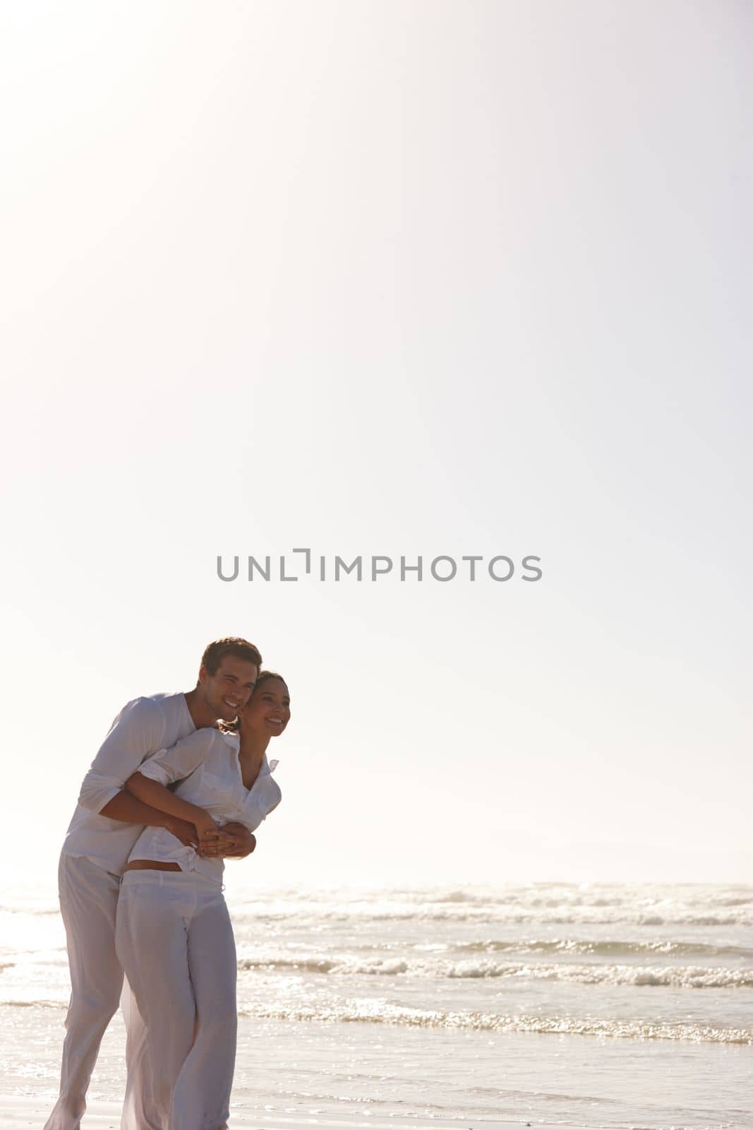 Having a romantic walk on the beach. a young couple embracing at the beach. by YuriArcurs