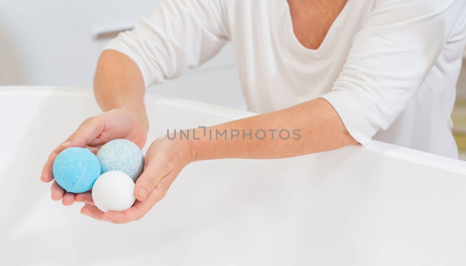 Closeup of a woman's hands with salt and soap balls in the bathtub for skin and body care. by PaulCarr