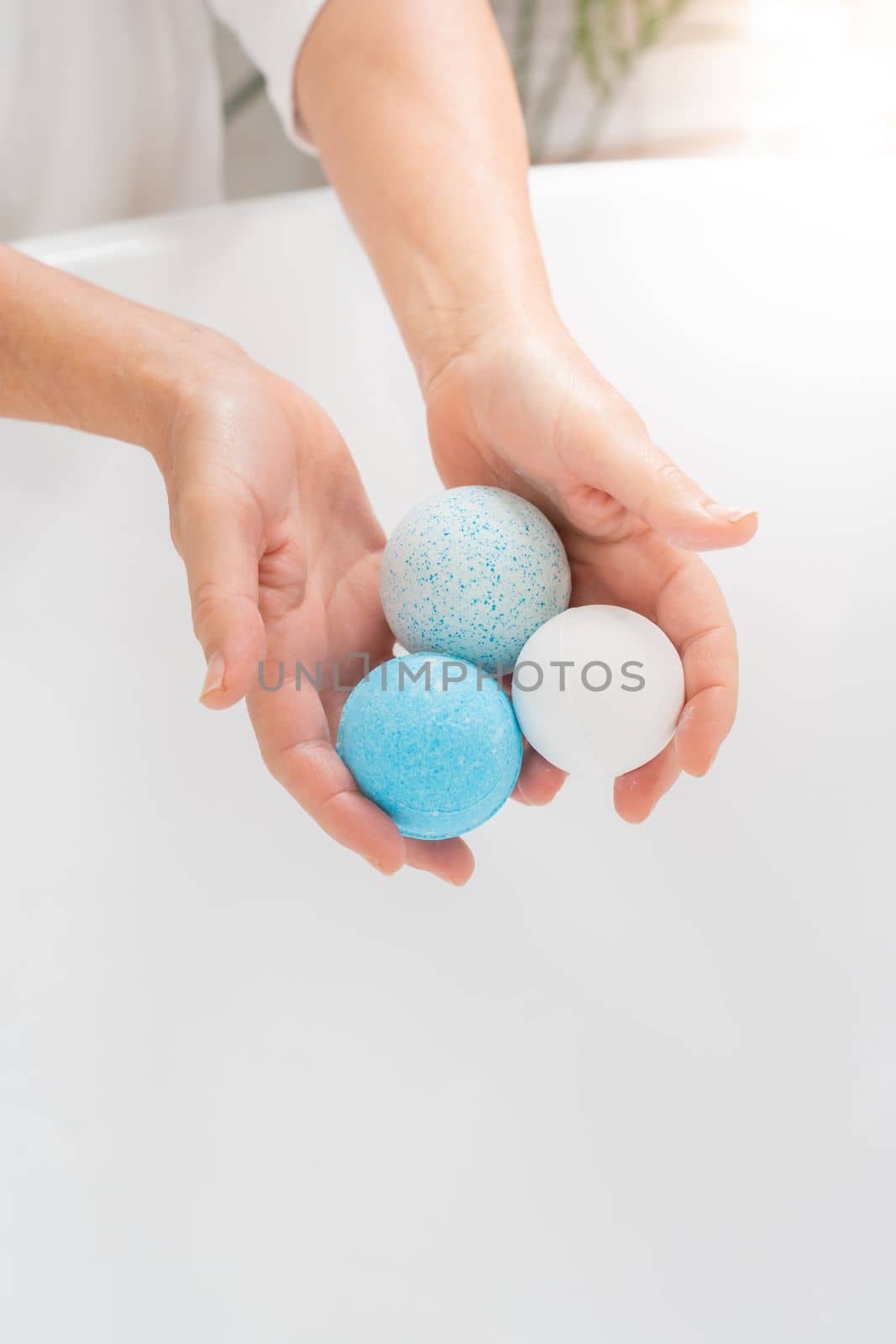 Vertical closeup of a woman's hands putting salt and soap balls in the bathtub for skin and body care.