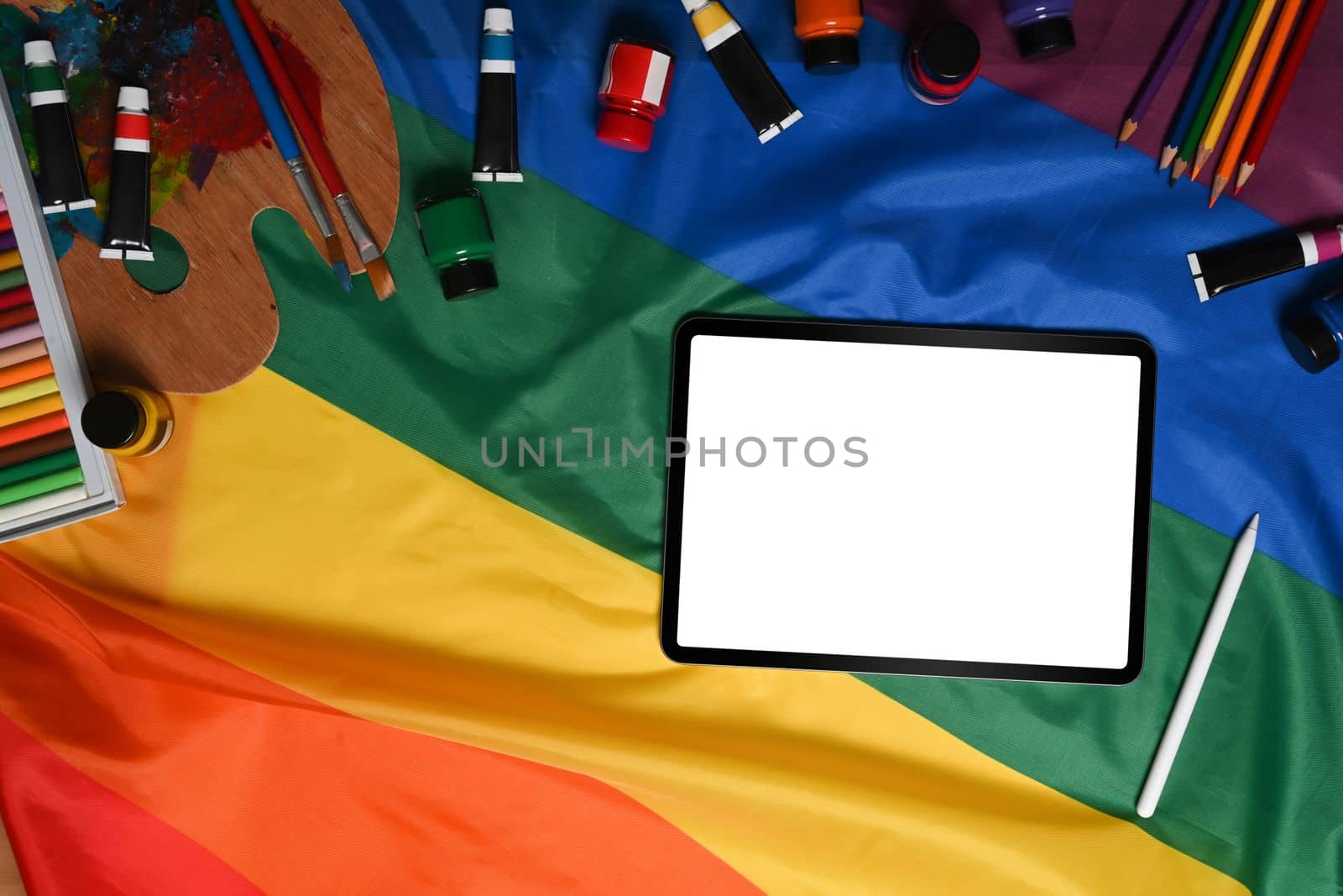 Digital tablet and artist tools over colorful rainbow flag. by prathanchorruangsak