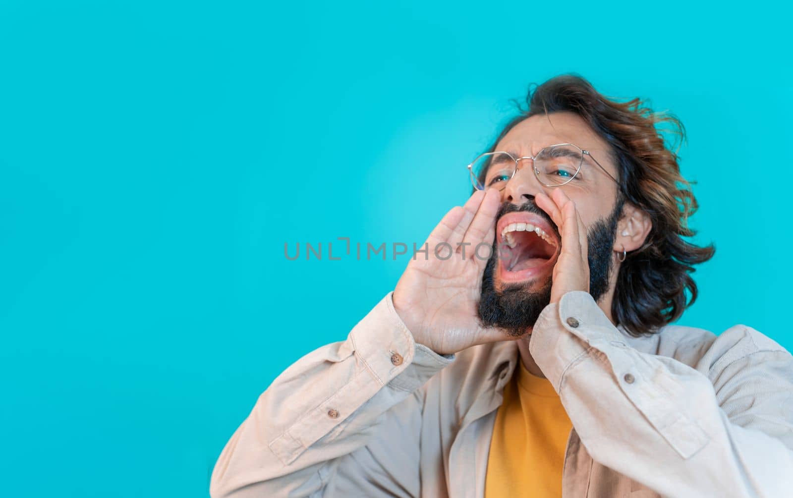 Man shouting loud calling attention with hands like megaphone isolated on blue studio background by PaulCarr