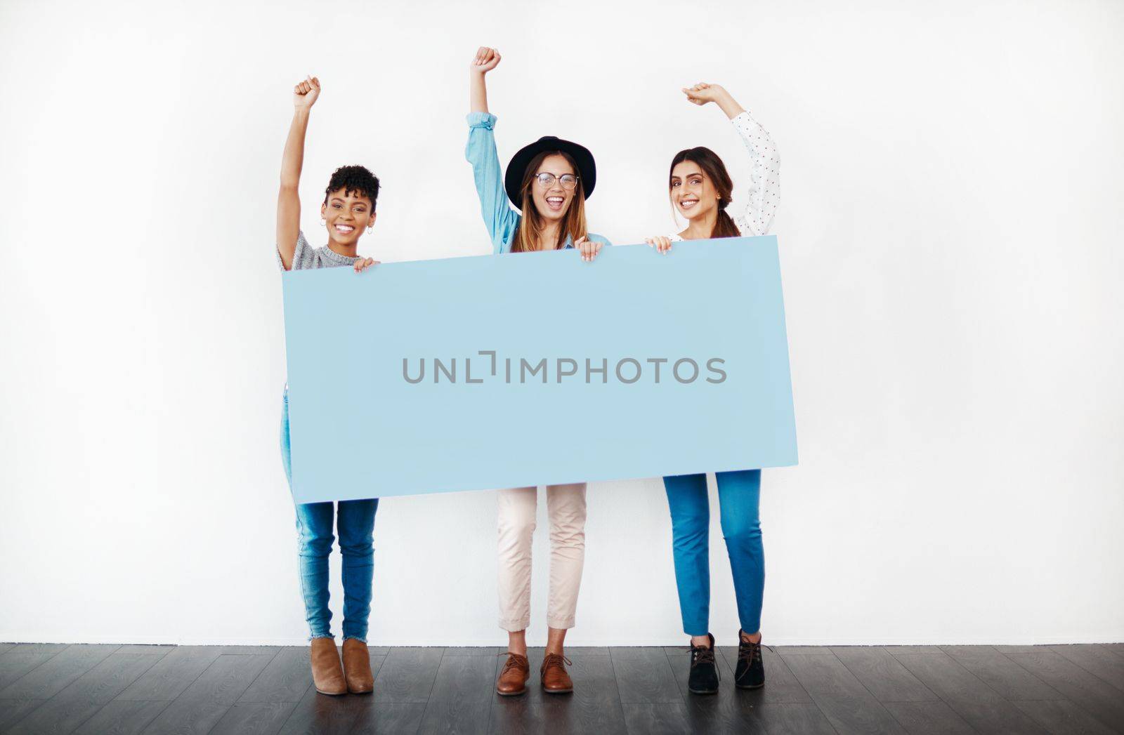 Shout out to women everywhere. Studio shot of a group of young women holding a blank placard and cheering against a white background. by YuriArcurs