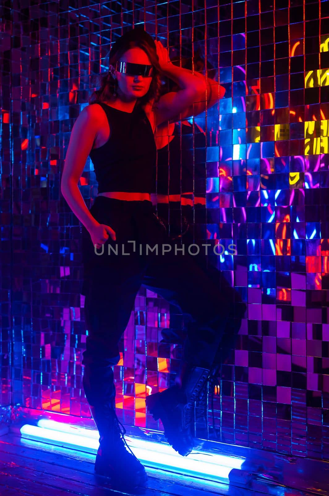 Portrait of a caucasian woman in sunglasses in neon light against a mirror wall