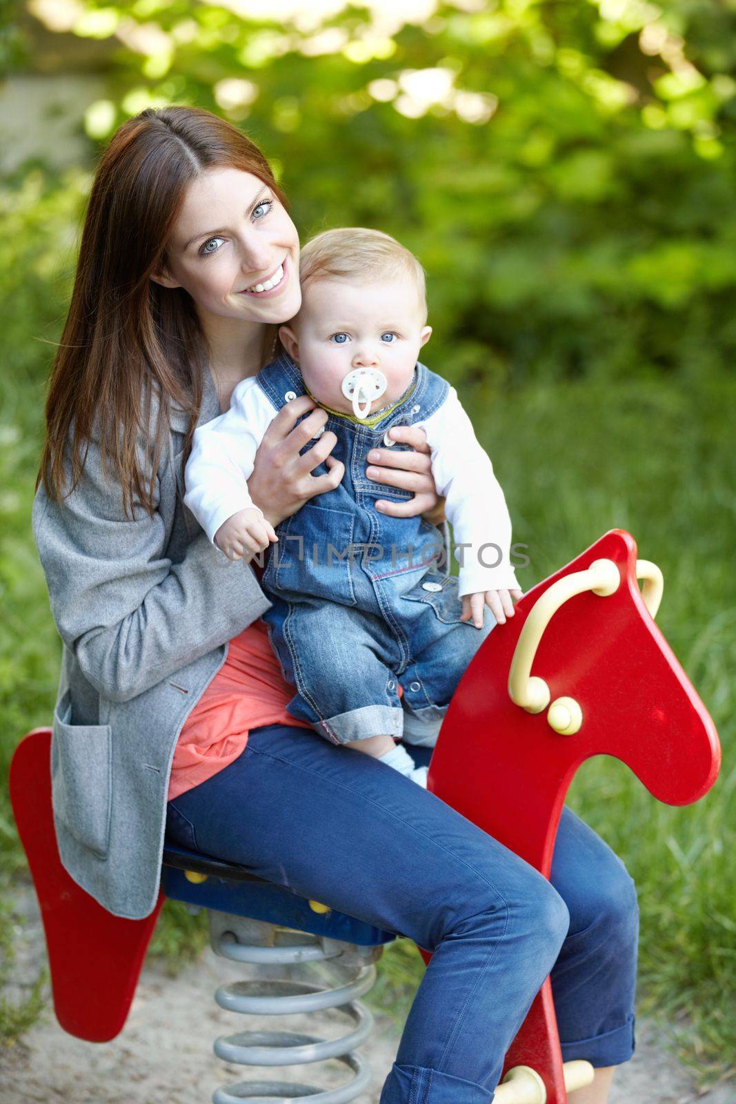 Building close bonds through playtime. Cute young mom on the bouncy horse with her baby son