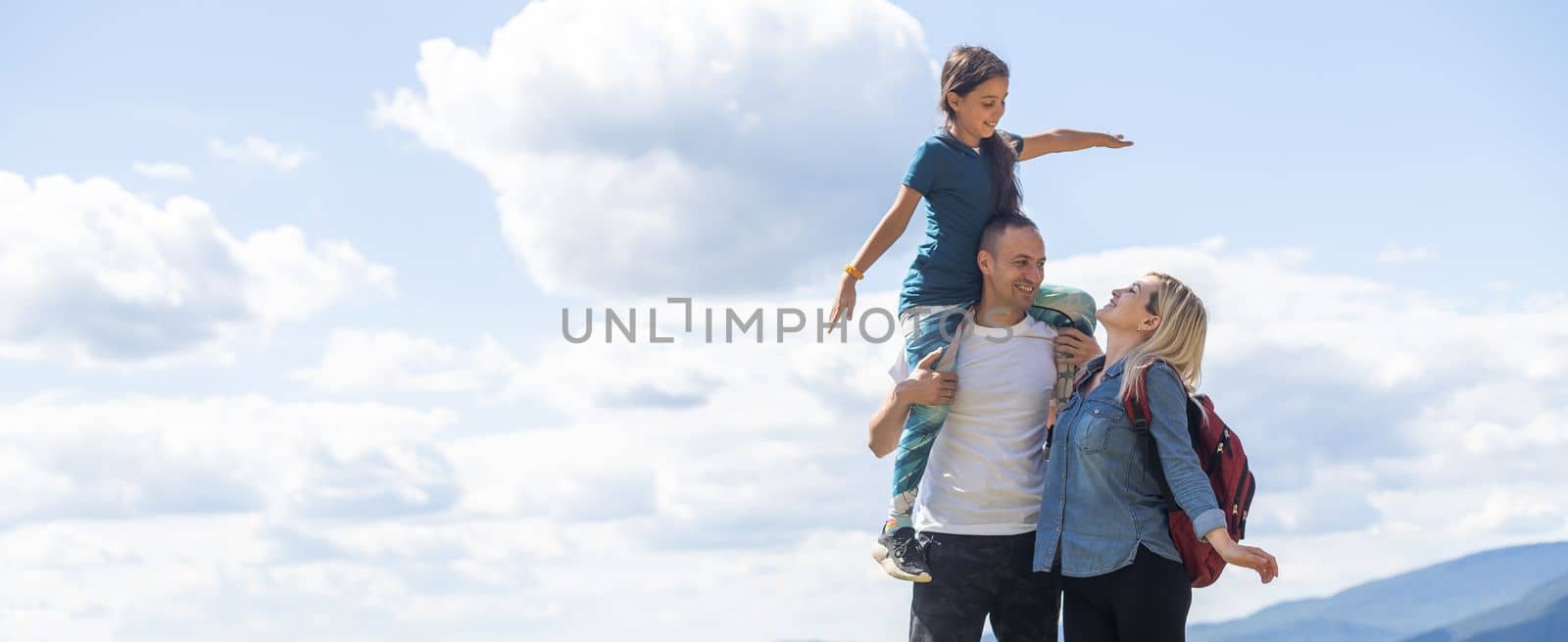Family standing with arms around on top of mountain, looking at beautiful summer mountain landscape. People enjoying view. by Andelov13