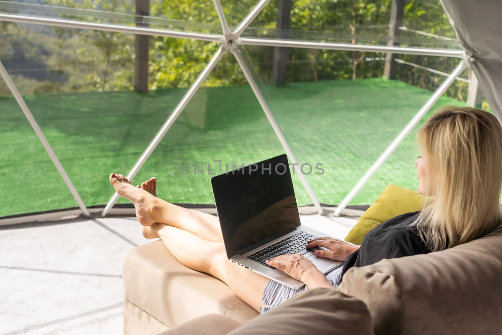 Happy young woman chatting online by using laptop in dome camping. Glamping vacation concept.