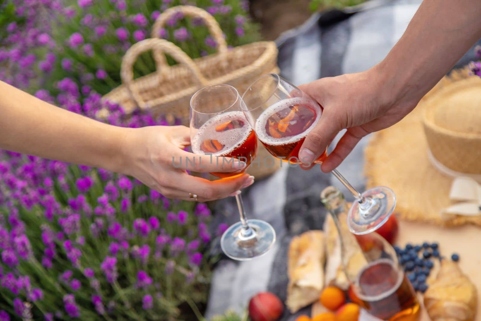 A man and a girl are holding glasses of wine on the background of a picnic in a lavender field. Selective focus
