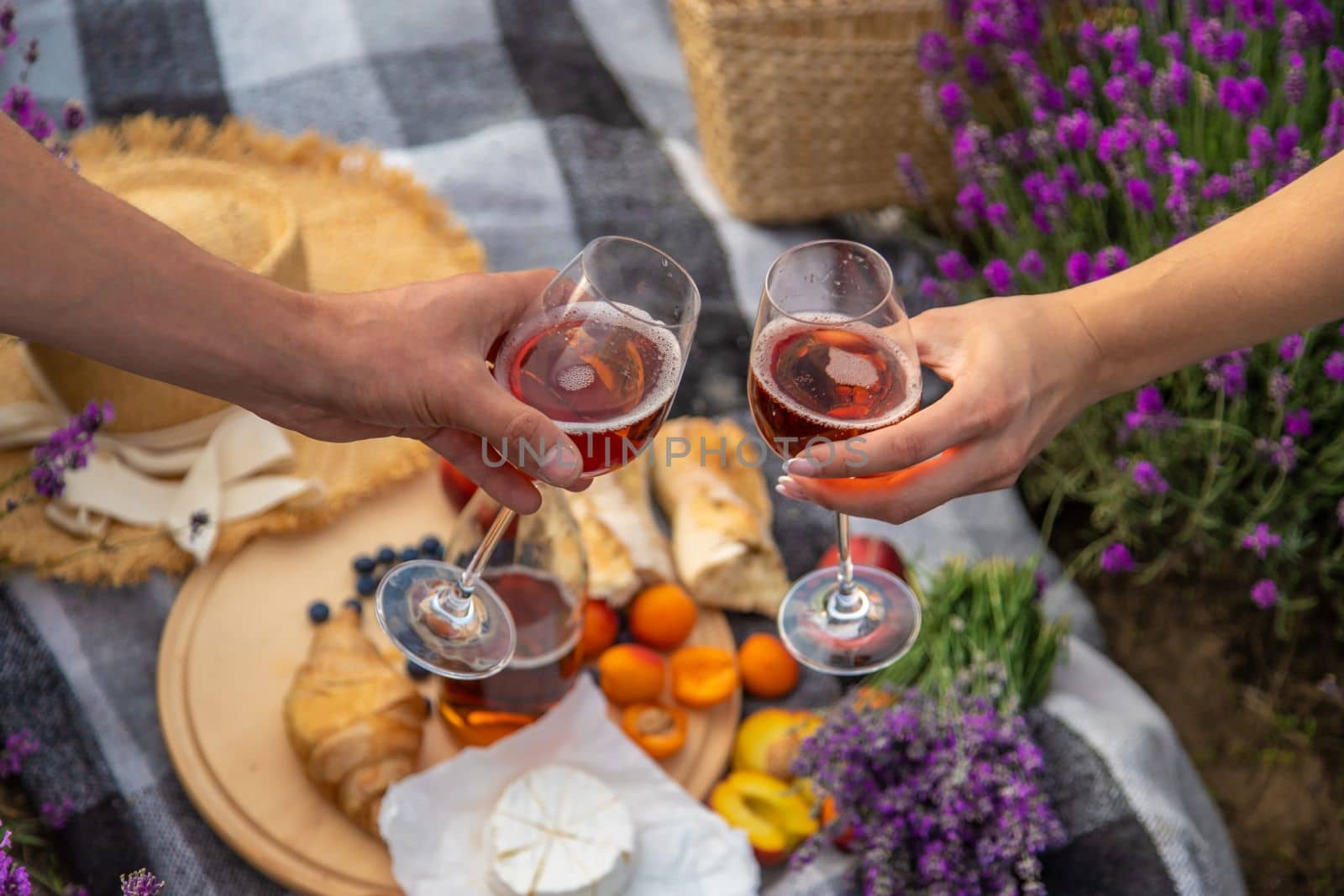 A man and a girl are holding glasses of wine on the background of a picnic in a lavender field. Selective focus