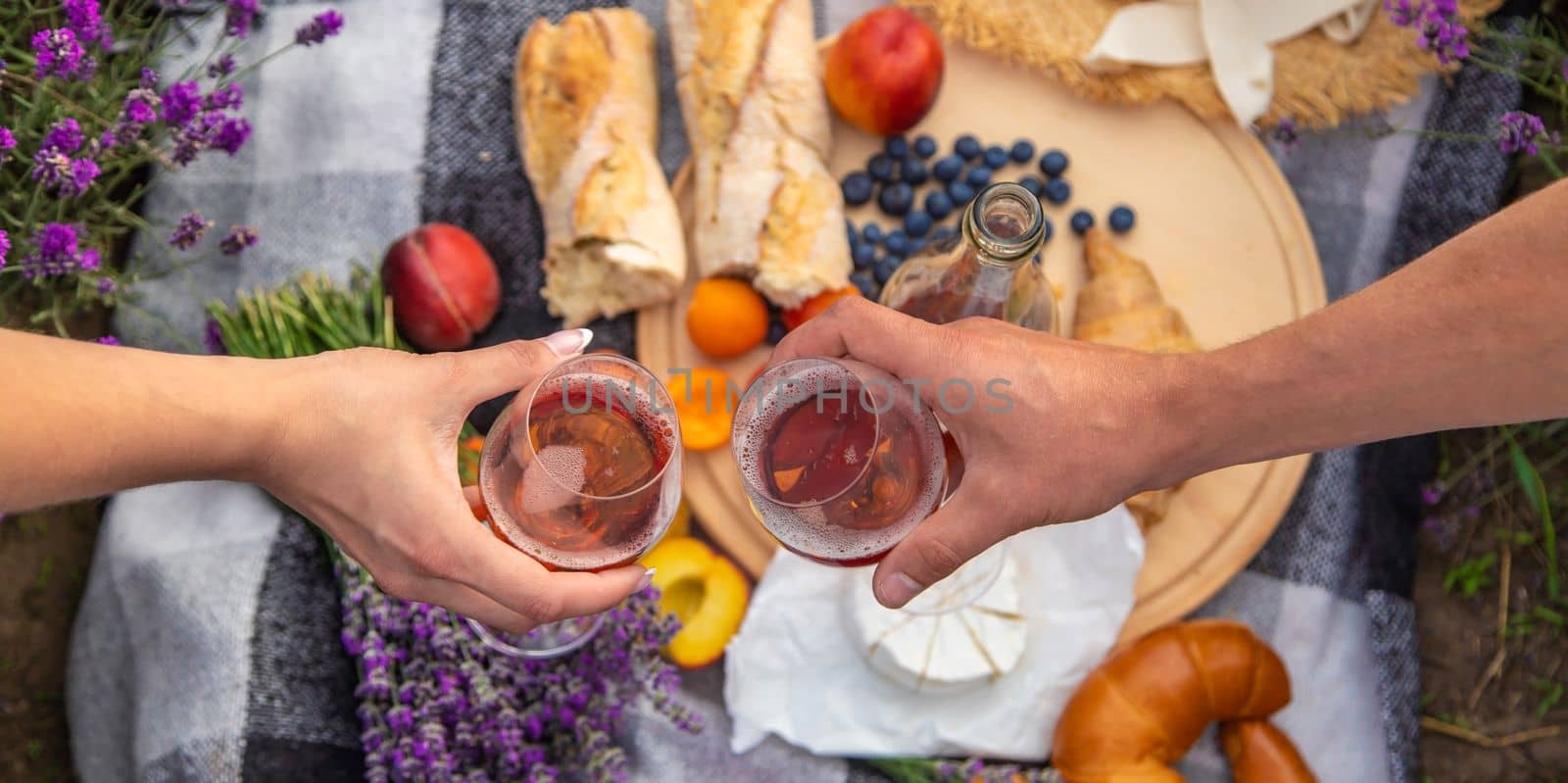 A man and a girl are holding glasses of wine on the background of a picnic in a lavender field. Selective focus