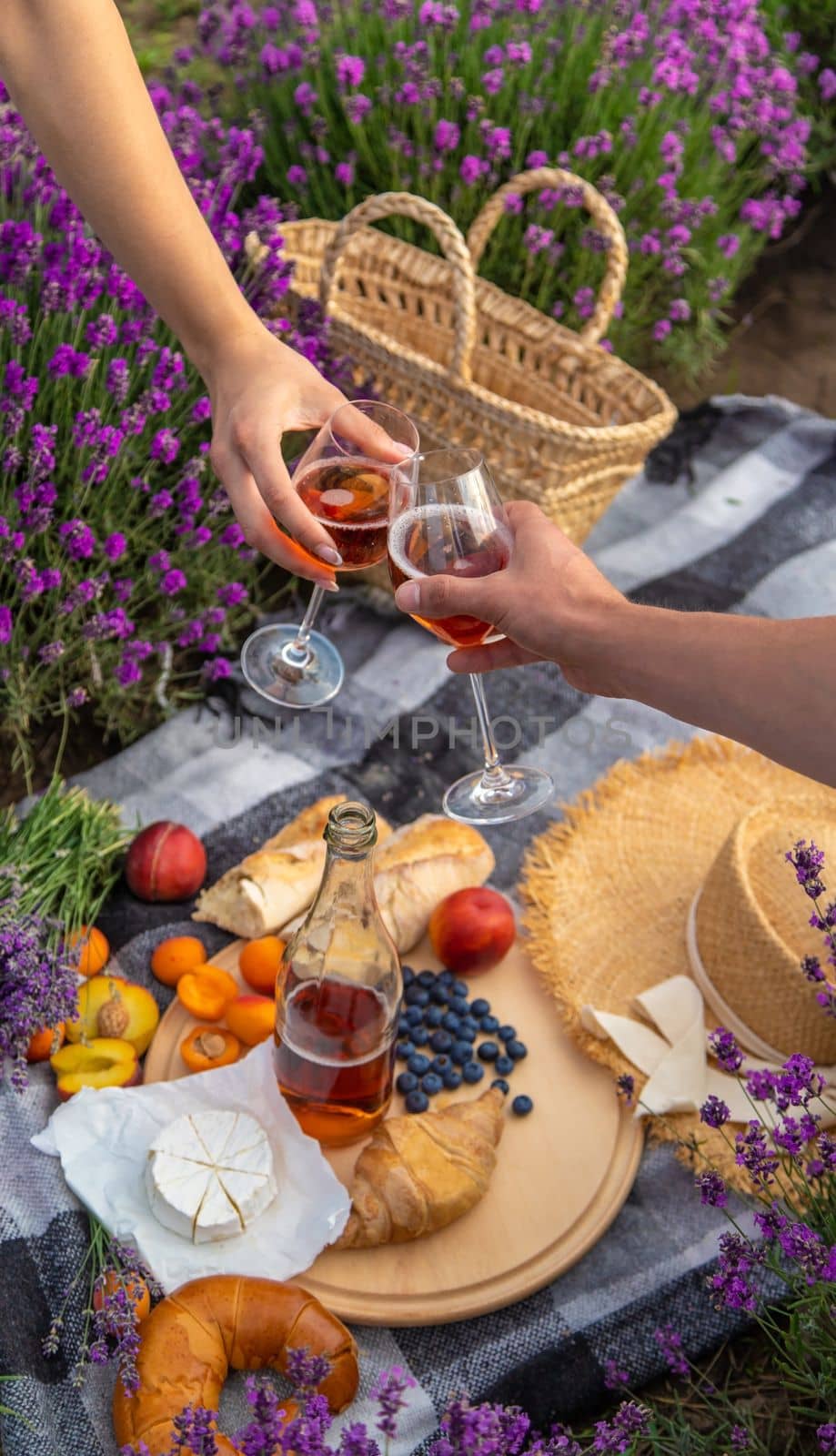 A man and a girl are holding glasses of wine on the background of a picnic in a lavender field. Selective focus