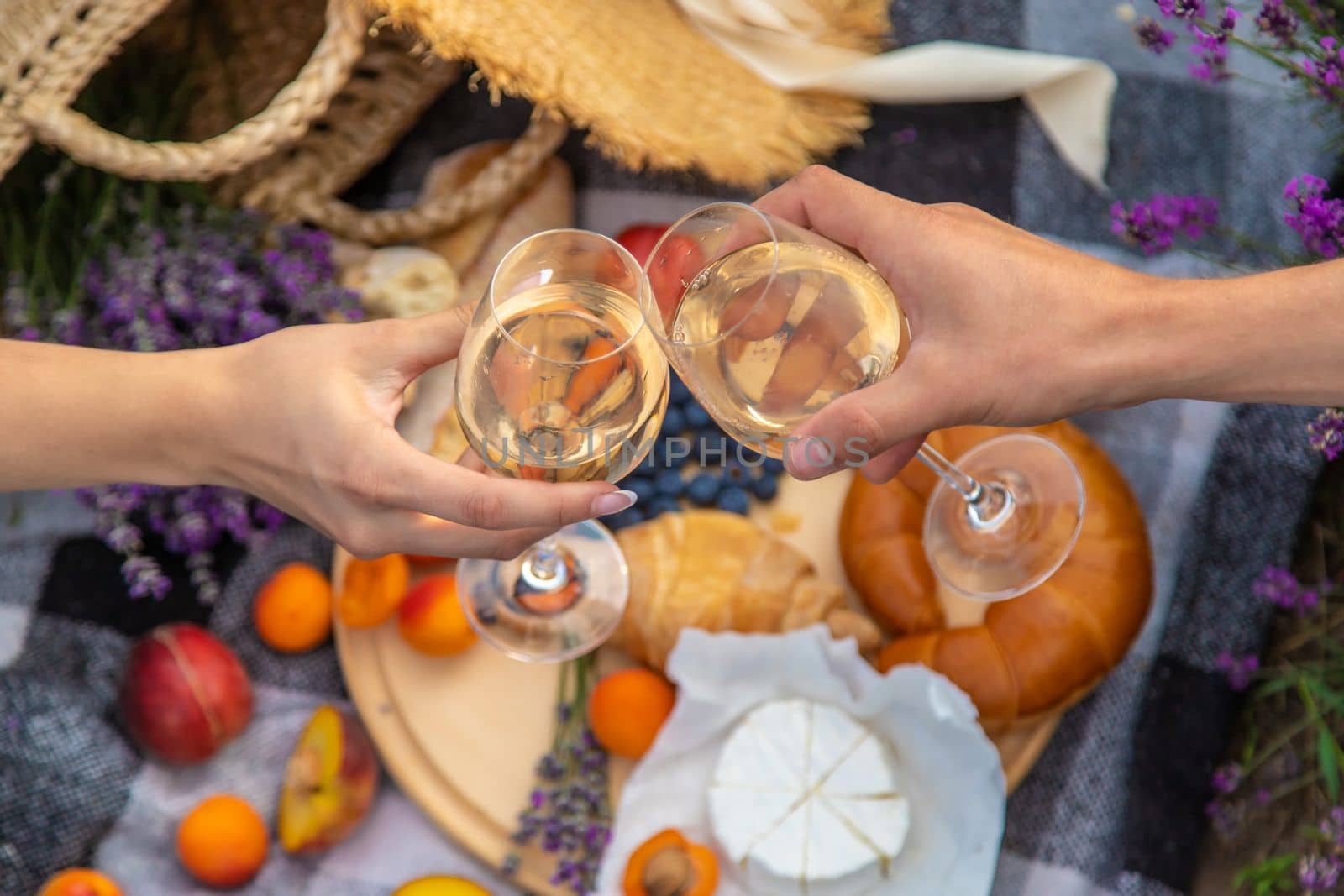A man and a girl are holding glasses of wine on the background of a picnic in a lavender field. Selective focus