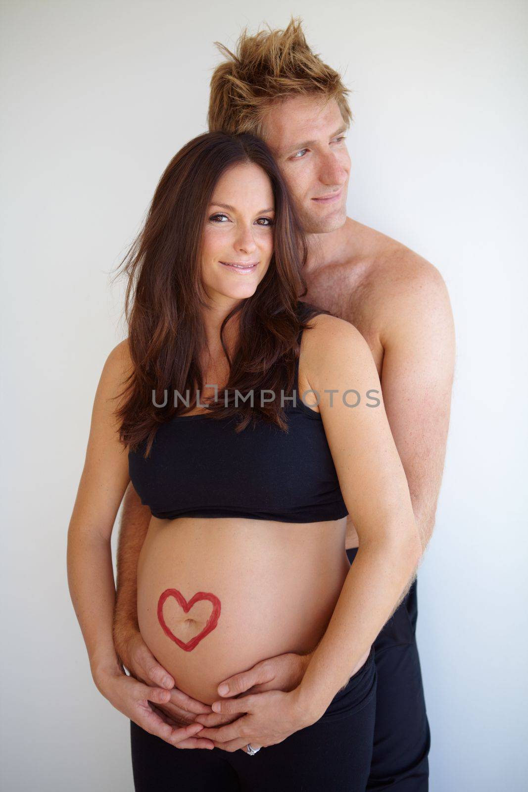 Sharing a bond that will never fade. Young expecting couple standing together with a heart shape on the expecting motheramp039s belly. by YuriArcurs