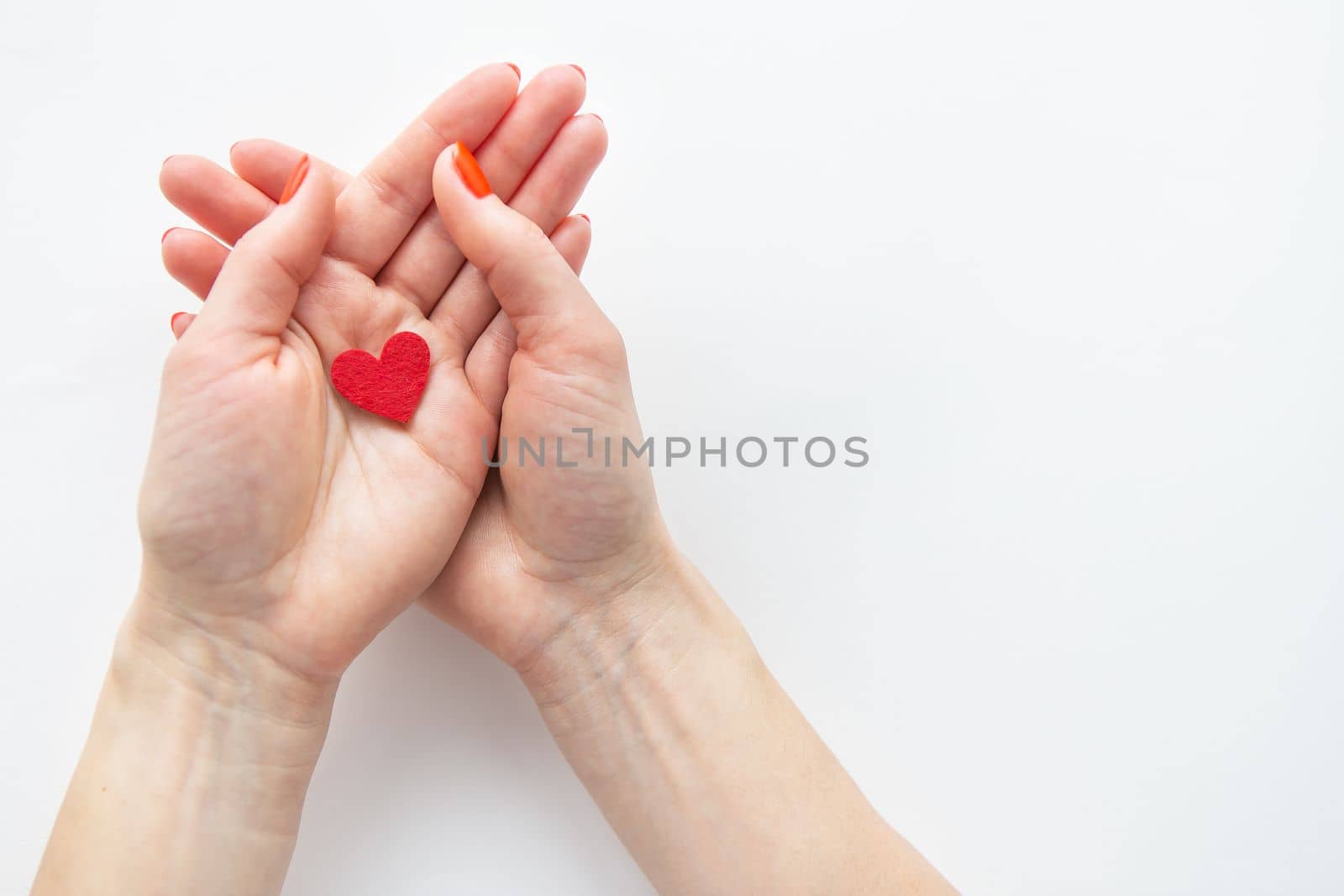 Female hands are holding a small red heart. The concept of care and love. by sfinks