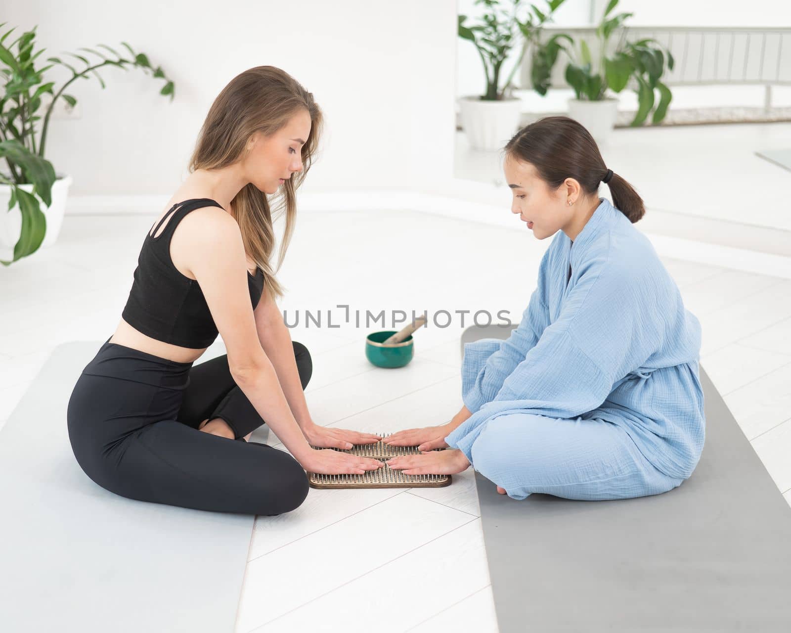 Two women sit on yoga mats with their hands on sadhu boards. by mrwed54