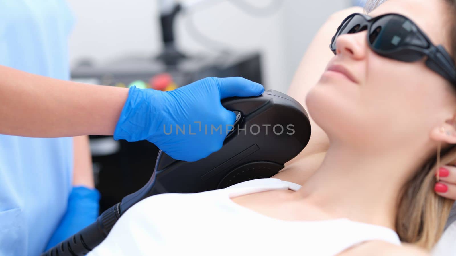 Beautician makes laser hair removal procedure in armpit area of young woman in clinic. Hair removal procedure with photoepilator or laser hair removal of armpits in salon
