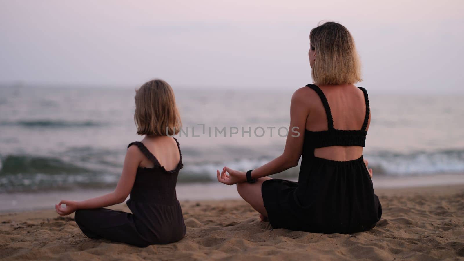 Woman with daughter on beach is doing yoga. Family relaxing yoga concept