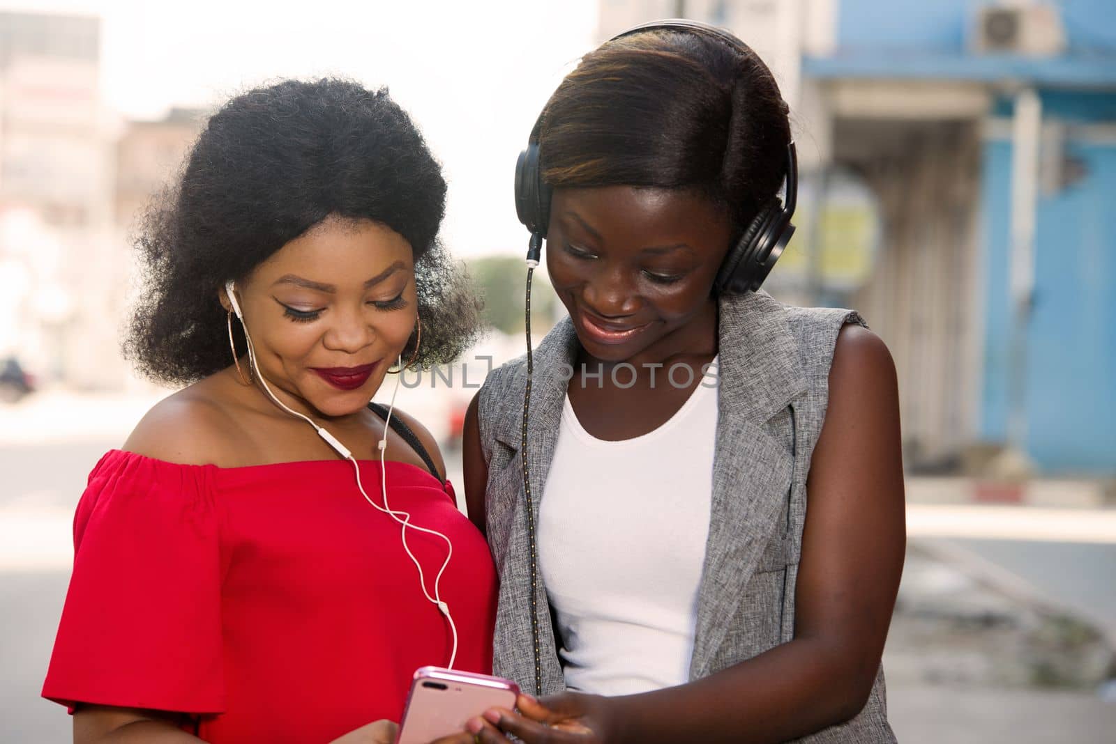Two beautiful and happy young women are smiling, talking and looking for something on a cell phone in the city