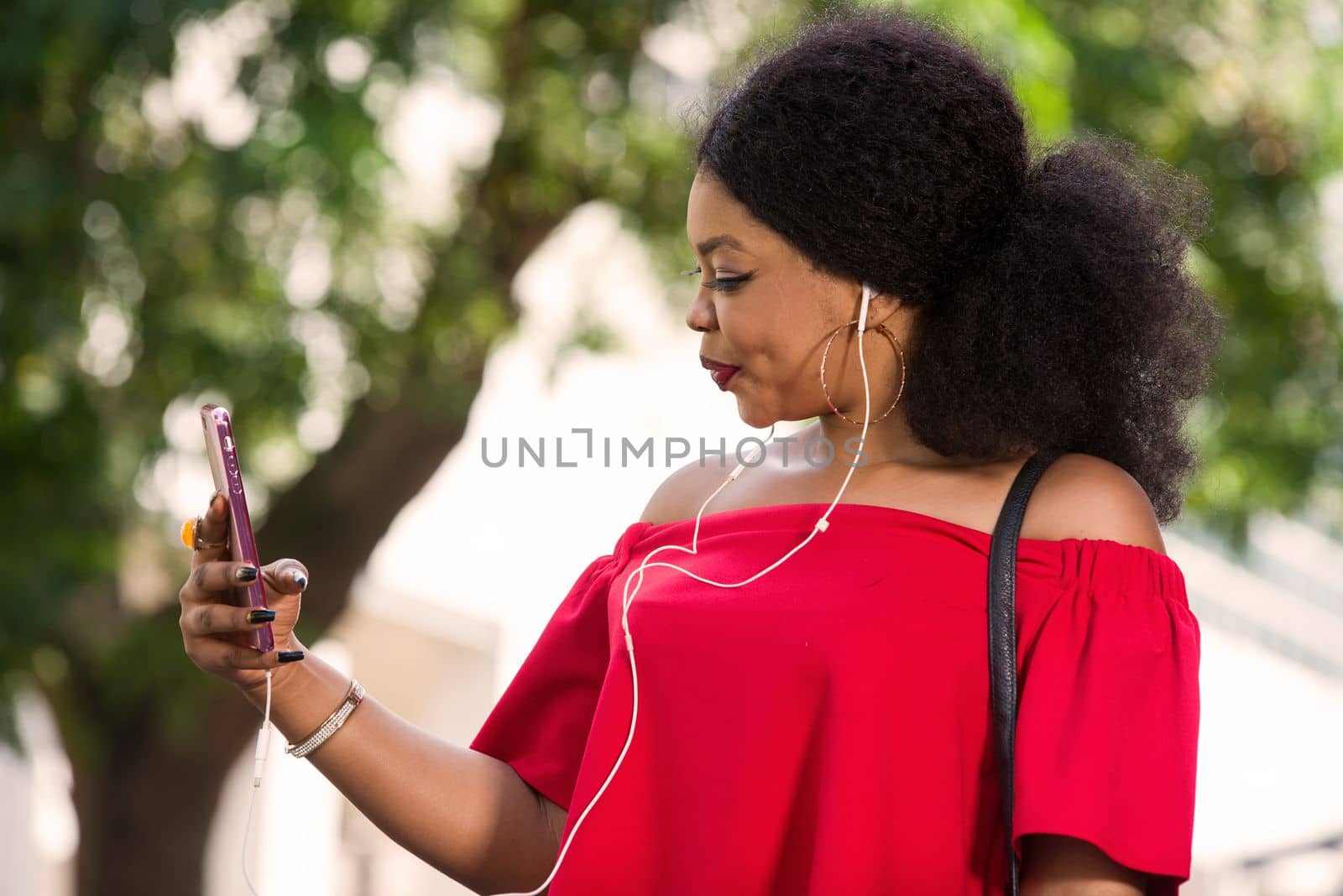 Happy young woman wearing a red t-shirt with headphones talking on the mobile phone in the city