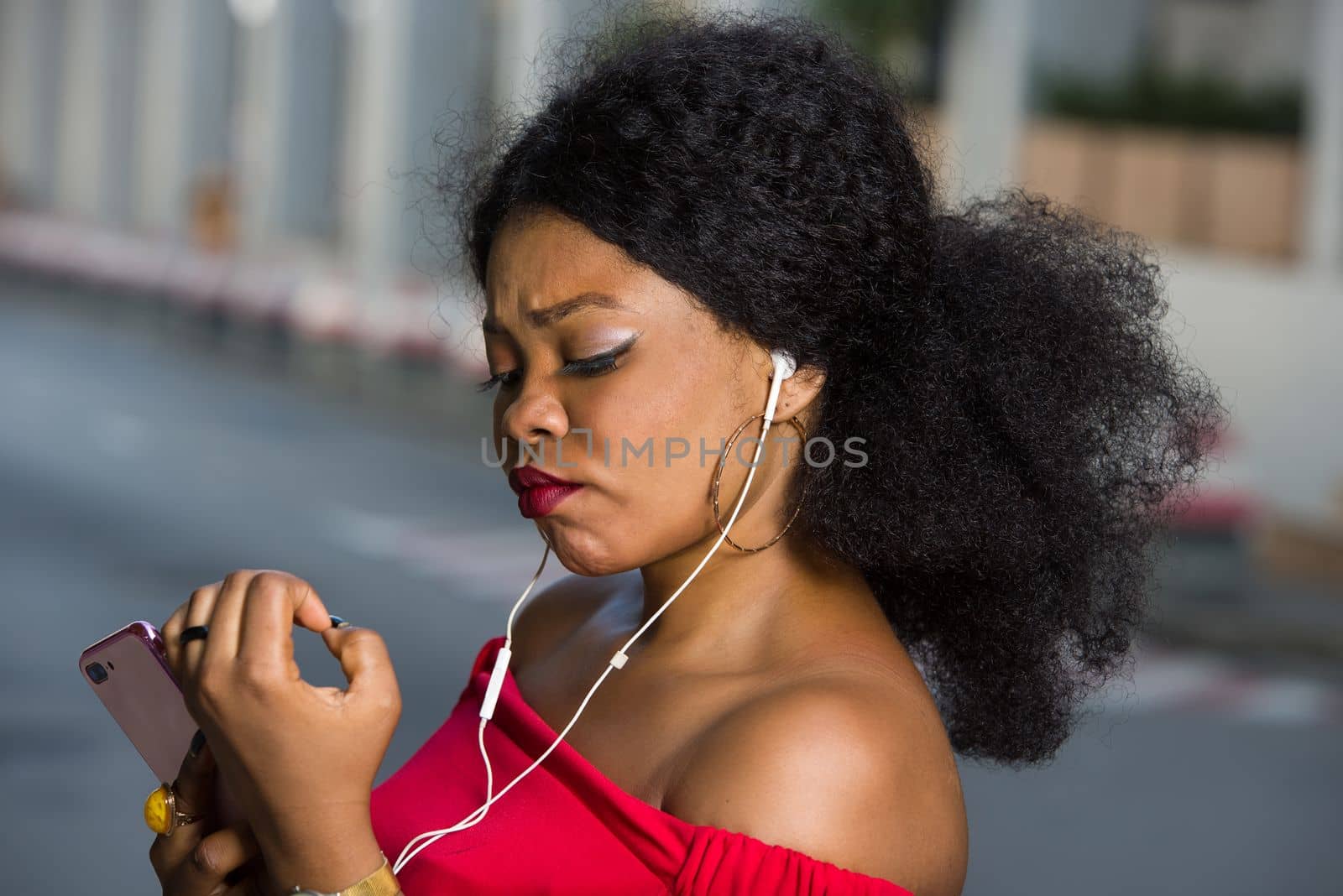 Pretty fashionable young woman talking on the phone checking her nail polish outdoors on a street