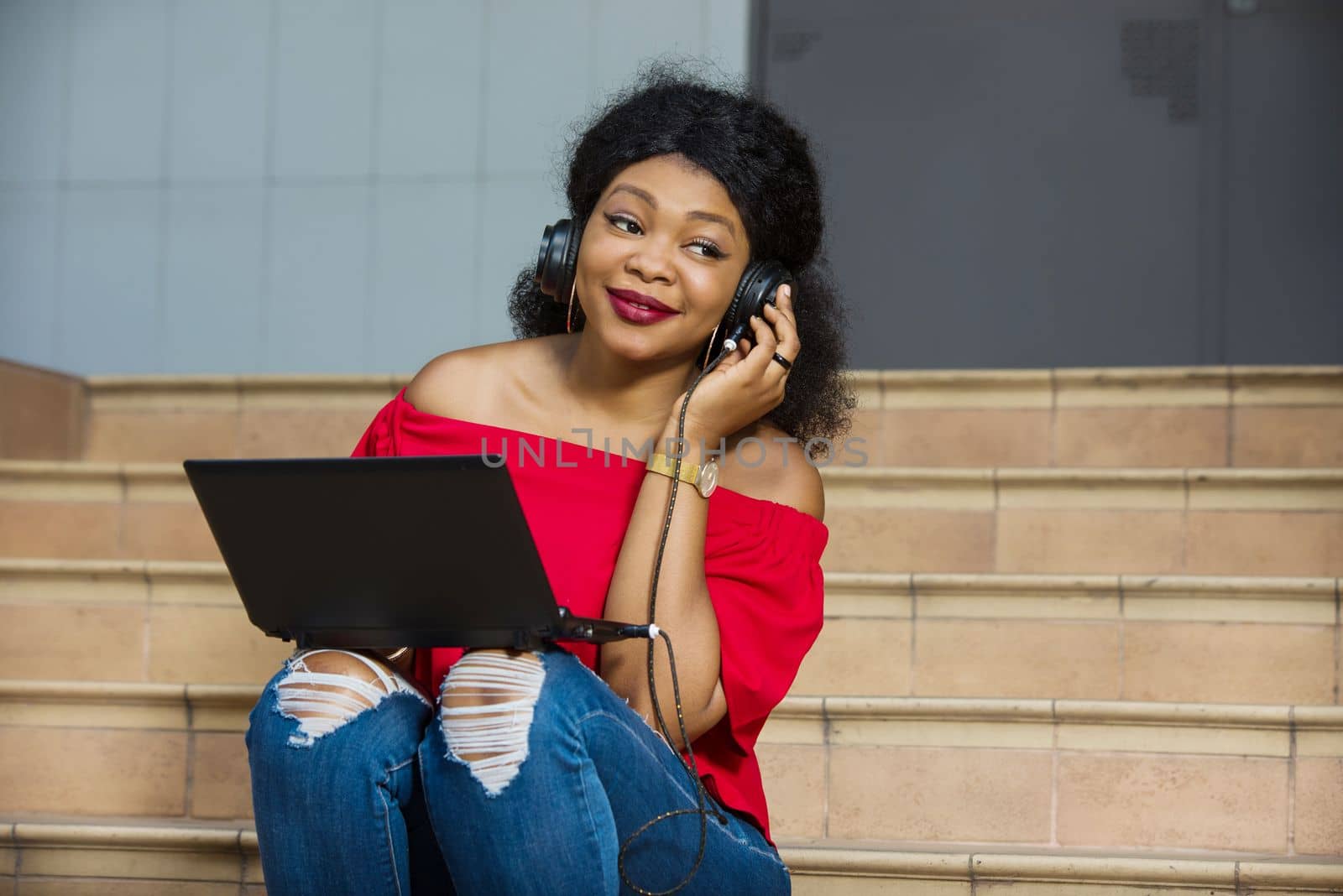 young girl sitting with laptop listening to music using headphones and looking at the camera smiling.
