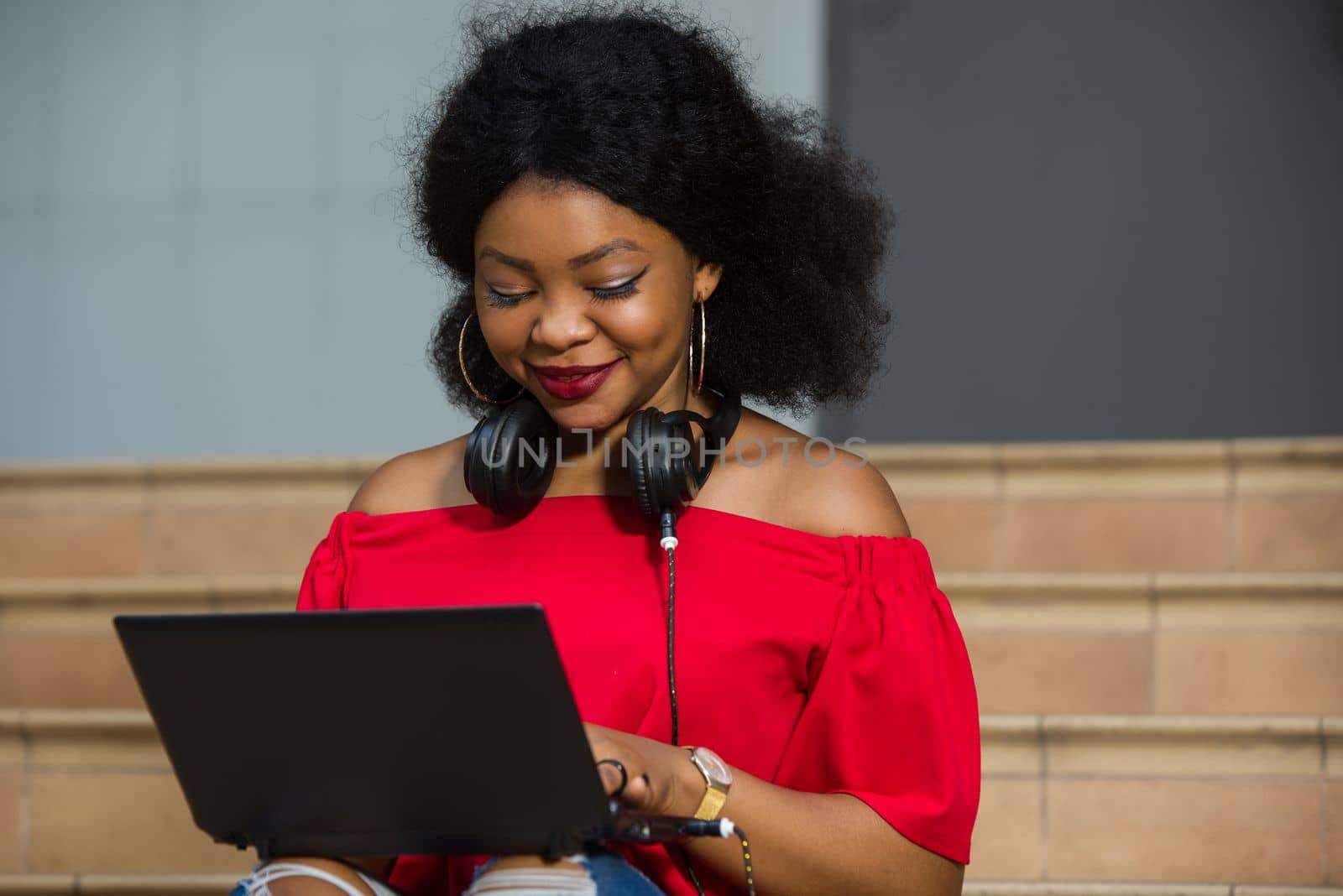 young girl sitting with headset at neck looking at laptop smiling.