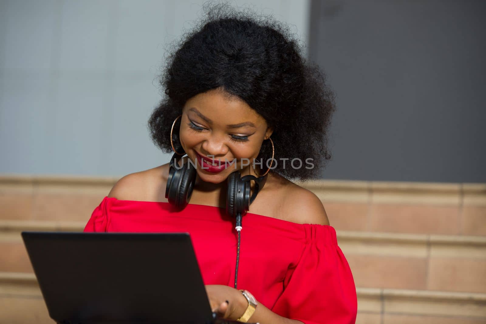 young girl sitting with headphones in the neck looking at laptop laughing.