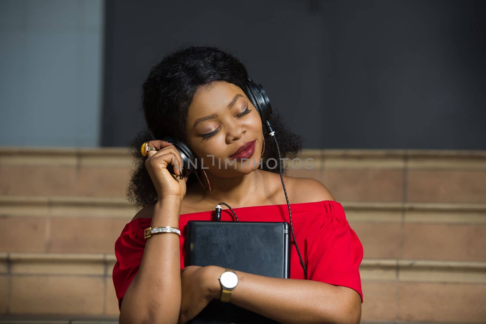 young girl sitting in red camisole with laptop listening to music using headphones closed eyes smiling.