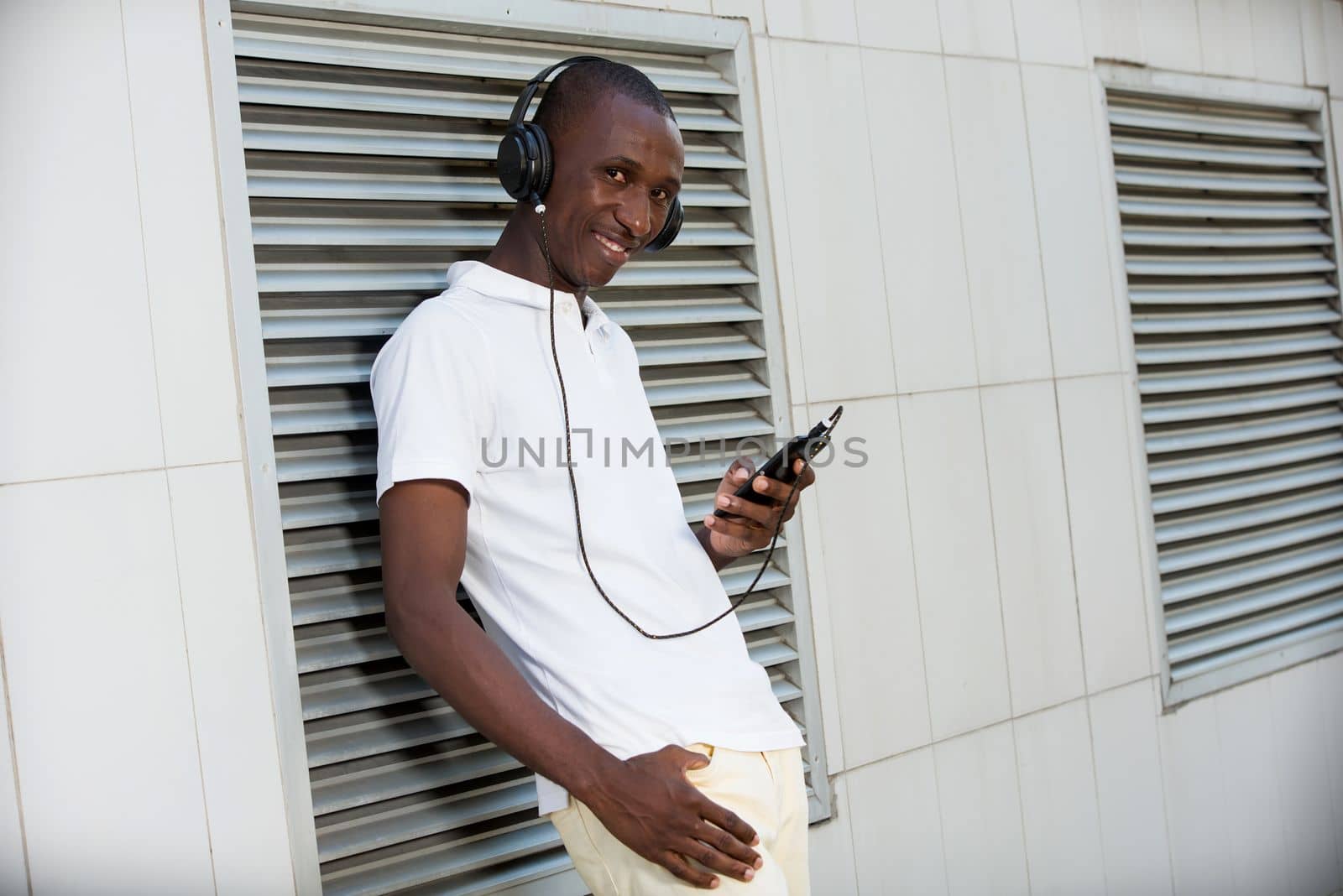 people, music, technology, leisure and lifestyle - Happy african young man with headphones and smart phone on the street