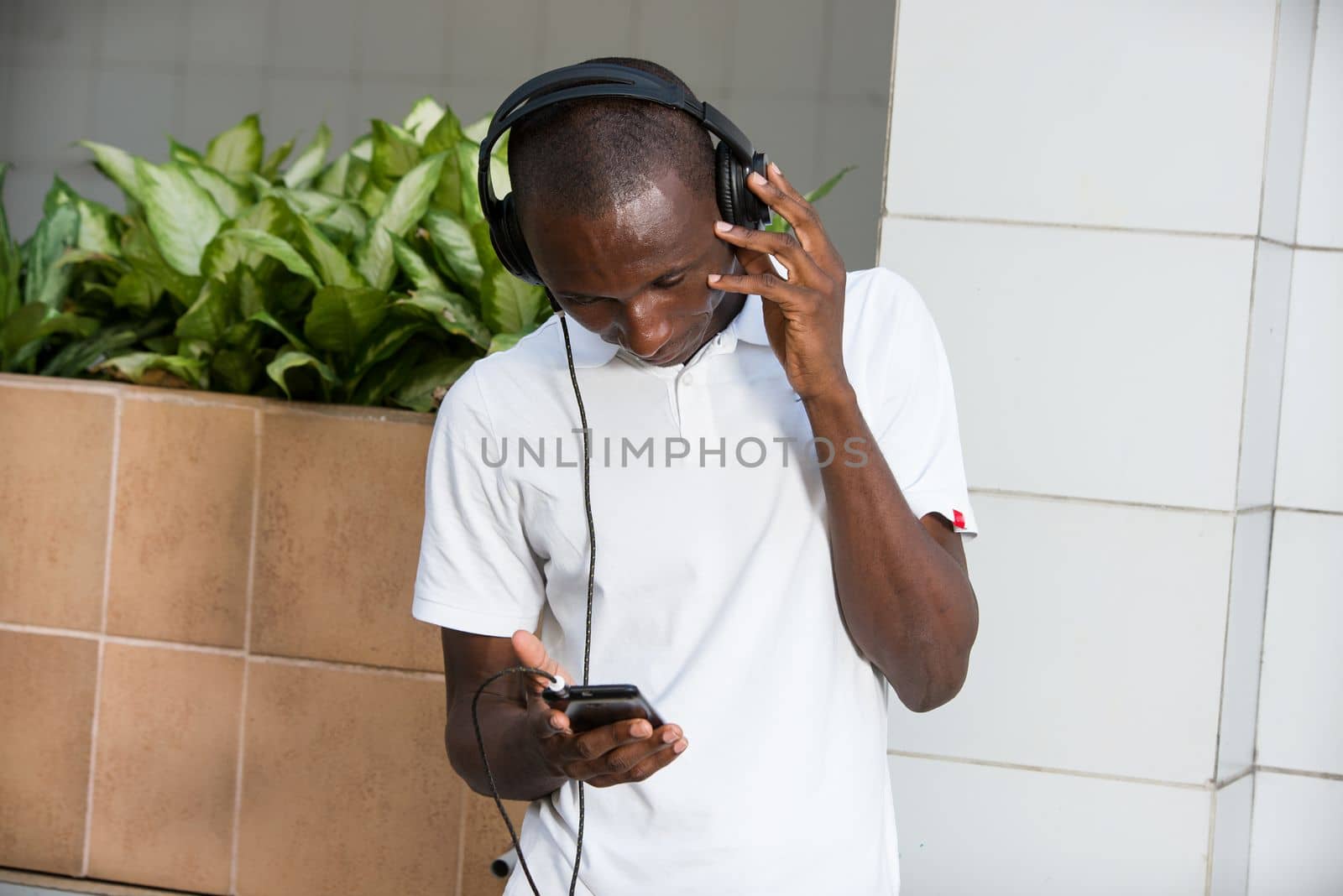 people, music, technology, leisure and lifestyle - Happy african young man with headphones and smart phone on the street