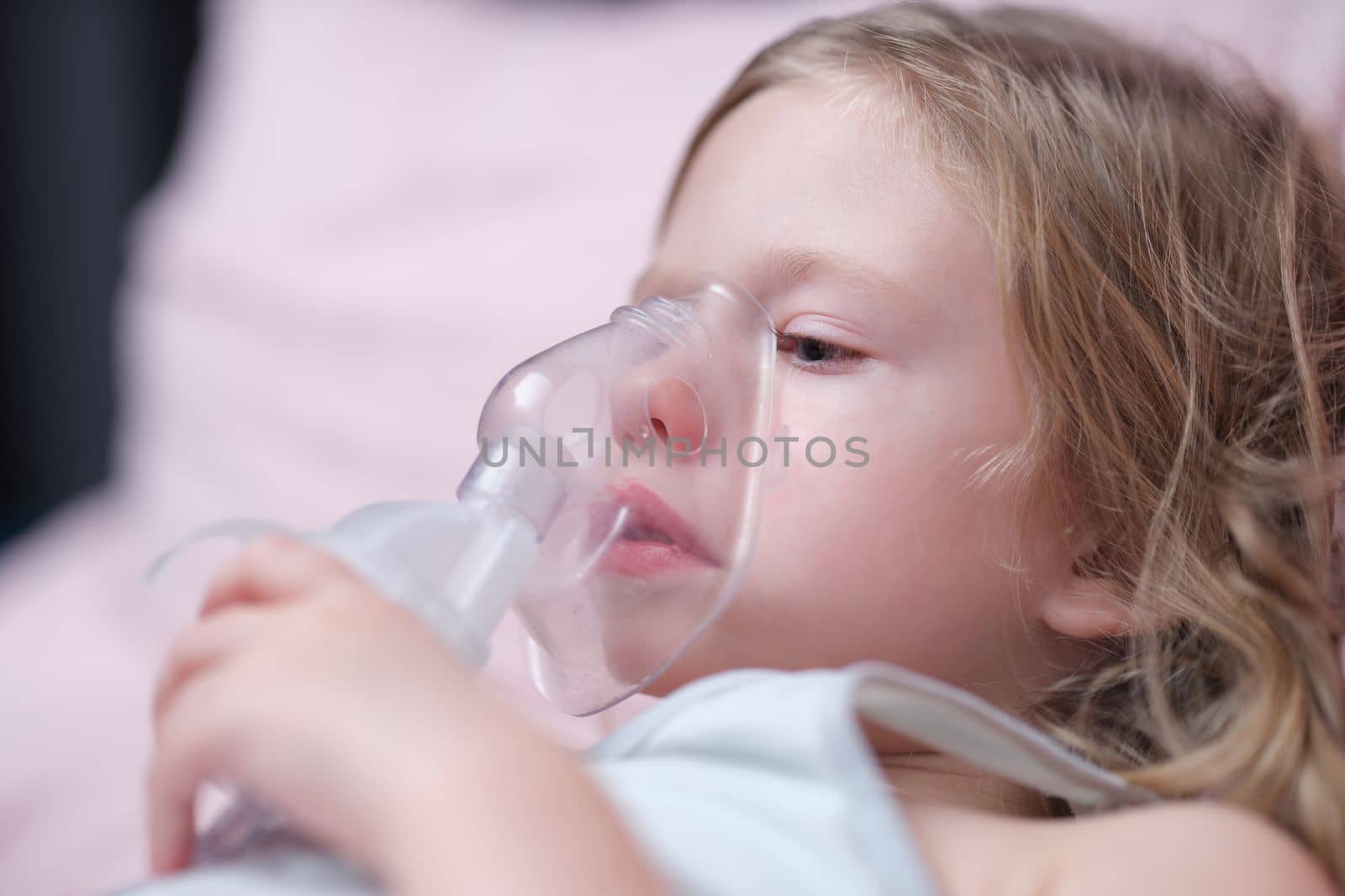 Oxygen mask of cute little girl on face on bed in hospital. Pneumonia asthma and nebulizer concept