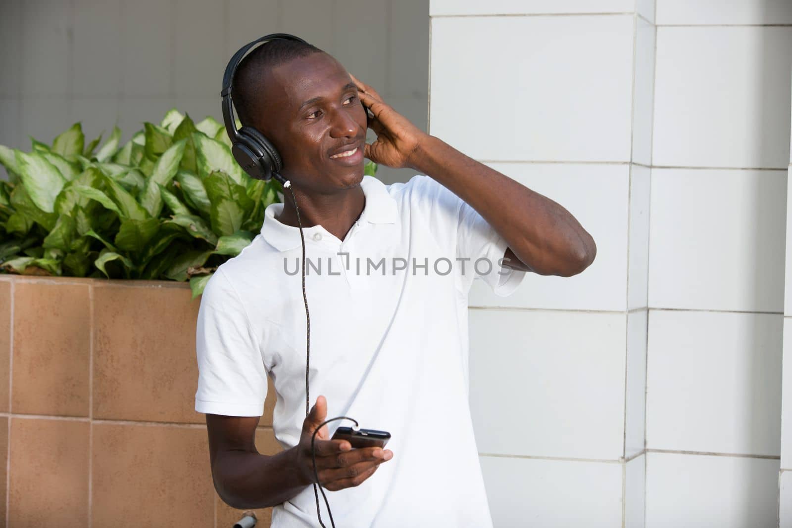 people, music, technology, leisure and lifestyle - Happy african young man with headphones and smart phone on the street