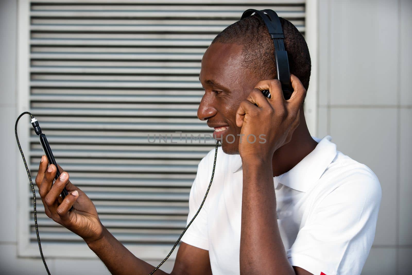 happy young man in white t-shirt listening to music with mobile phone headset and singing outdoors. Student with smart phone and headphones