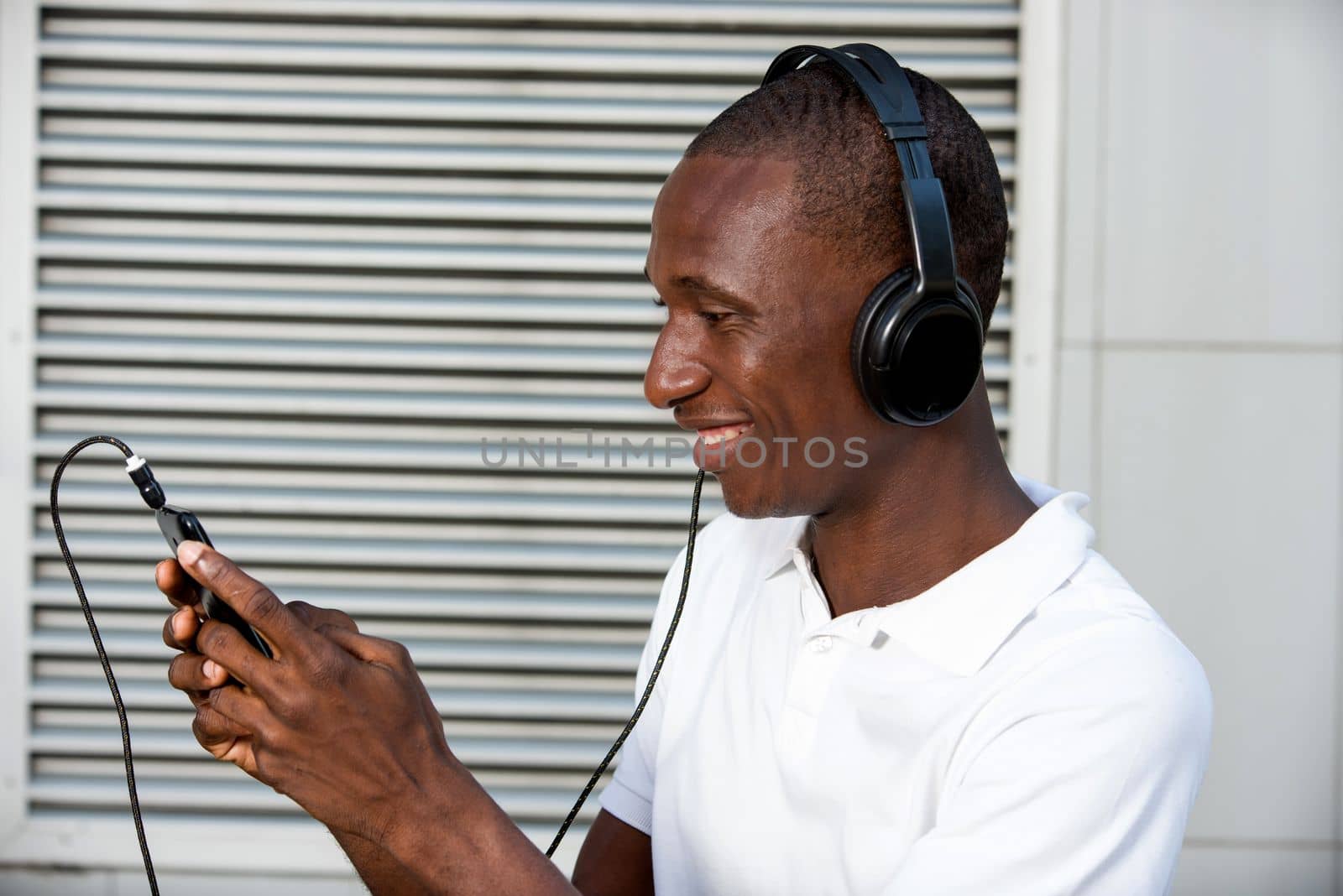 happy young man in white t-shirt listening to music with mobile phone headset and singing outdoors. Student with smart phone and headphones
