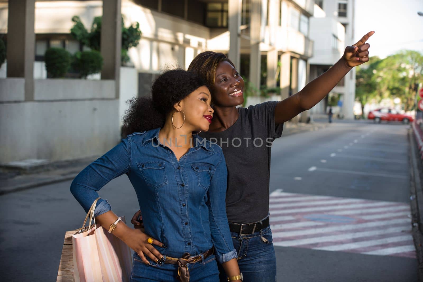 two happy young women holding shopping bags pointing a place with their finger in the city