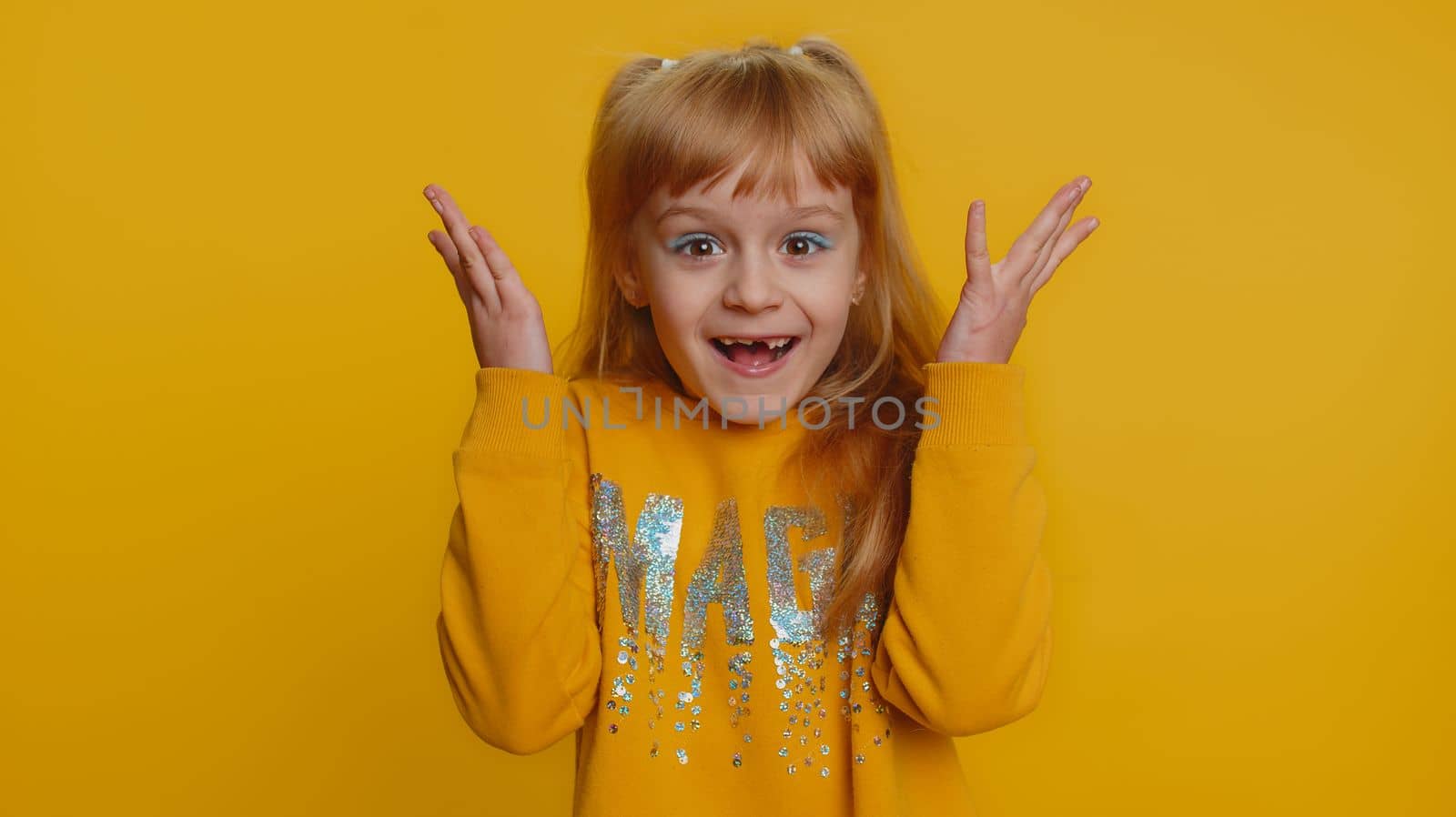 Oh my God, Wow. Young preteen child girl kid looking surprised at camera with big eyes, shocked by sudden victory, game winning lottery goal achievemen good news. Toddler children on yellow background