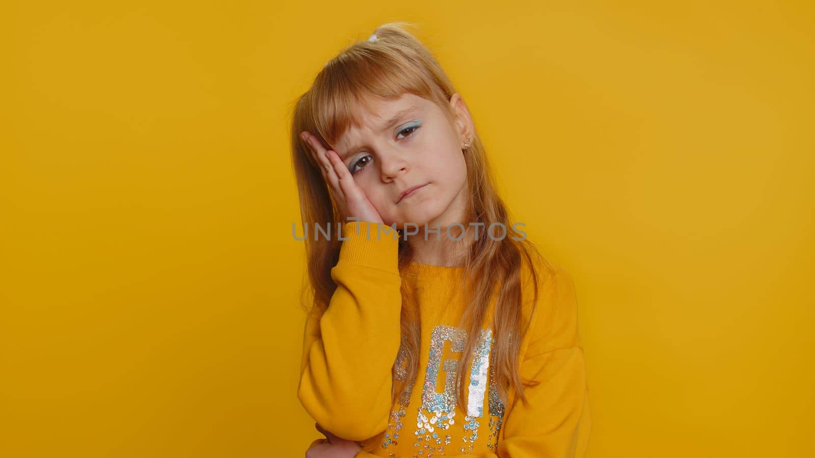 Displeased child girl kid rubbing temples to cure headache problem, suffering from tension, migraine, stress, grimacing in pain tired from study education. Little toddler children on yellow background
