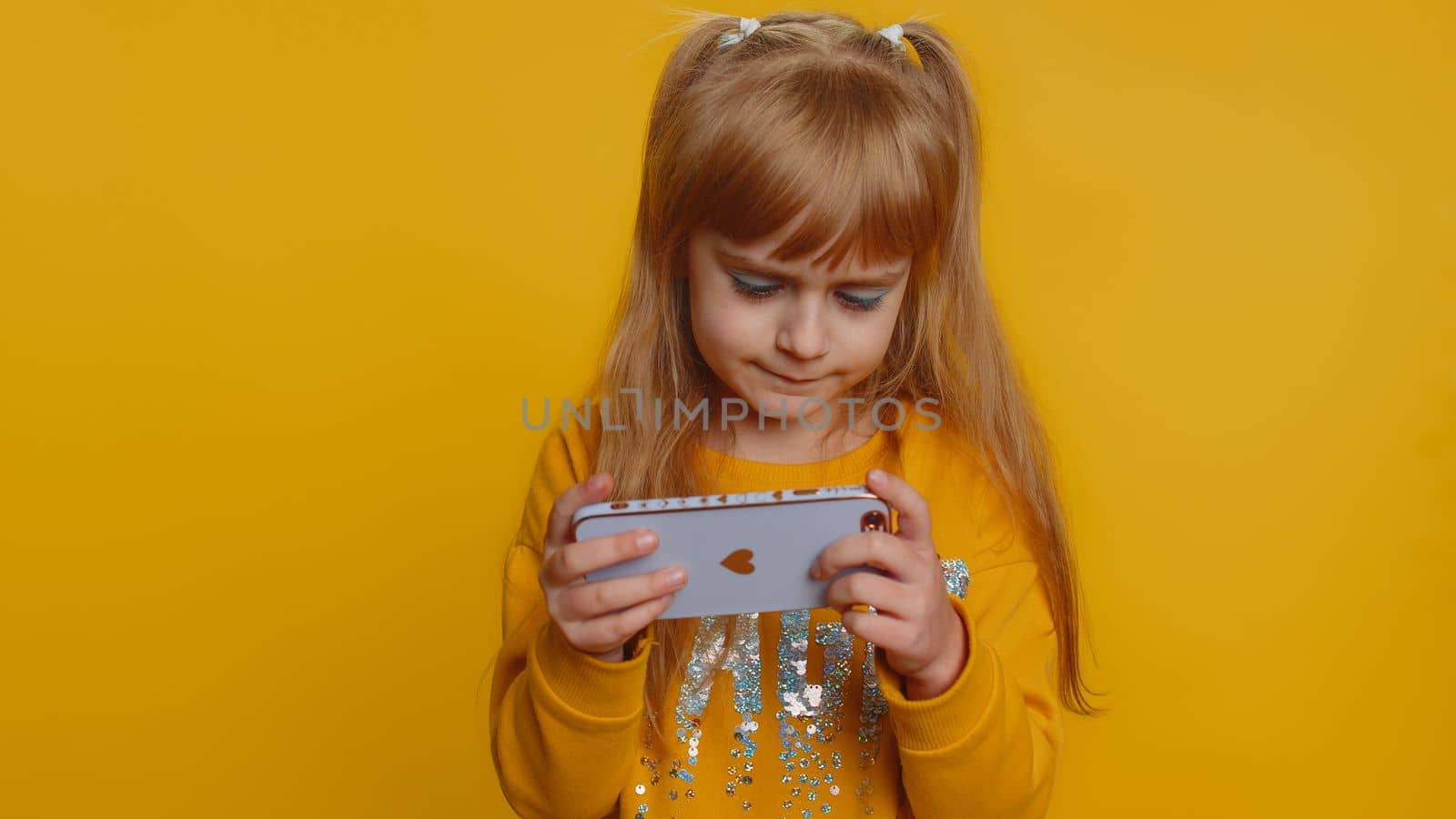 Worried funny young preteen child girl kid enthusiastically playing racing or shooter video games on smartphone. Excited little cute toddler children using mobile phone gadget app with drive simulator