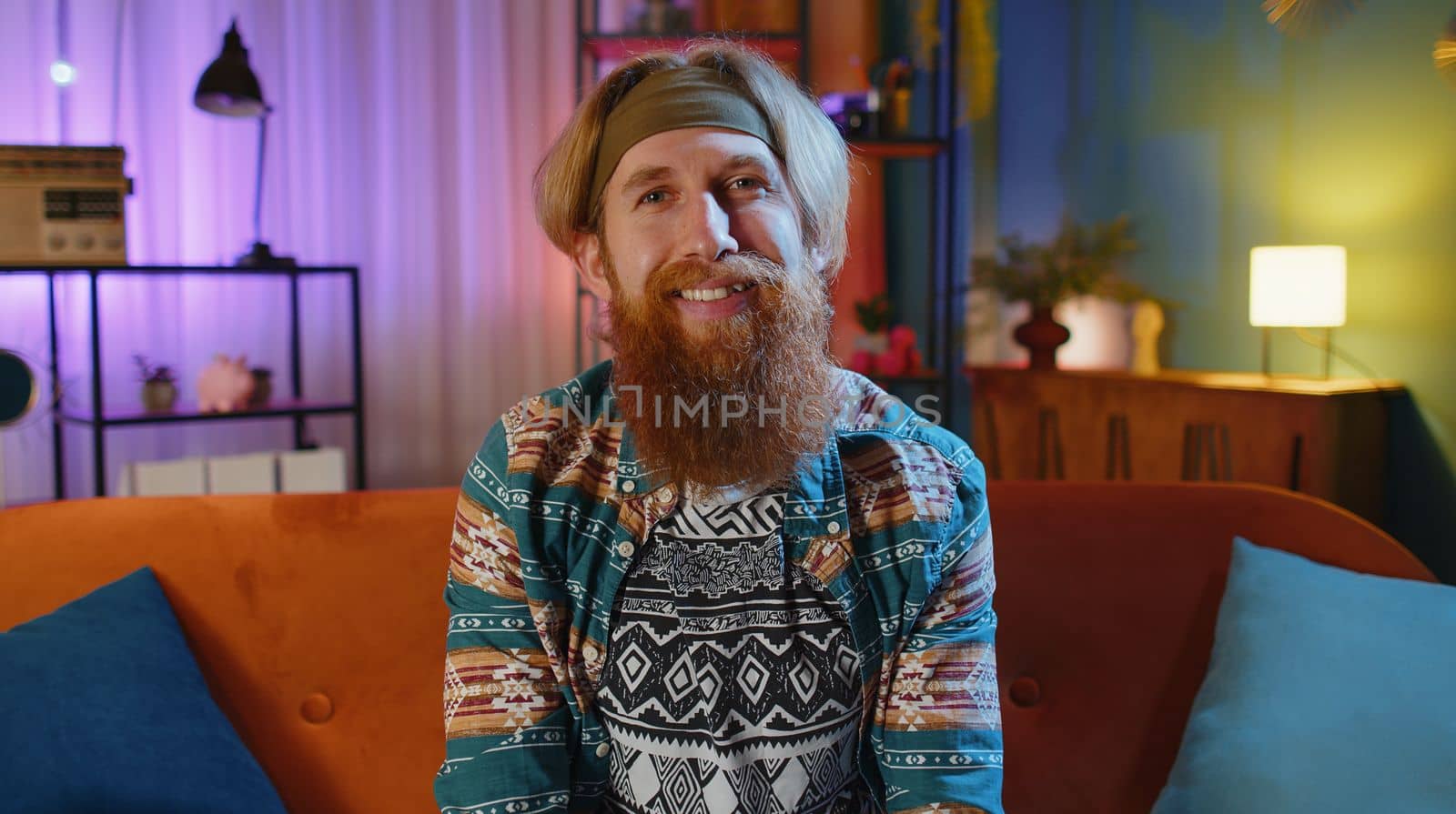 POV of bearded hippie redhead man at home couch looking at camera, making video webcam conference call with friends or family, enjoying pleasant conversation. Young hipster guy in night evening room