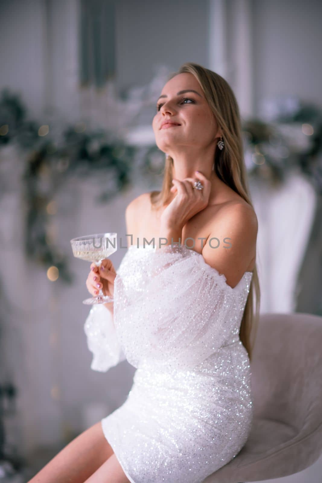 The blonde in the Christmas room. A beautiful blonde woman in a shiny light short dress with a train stands in a beautiful bright room decorated with a festive interior with a Christmas tree