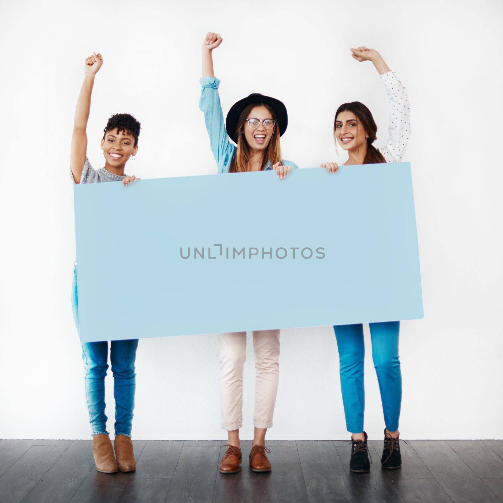 Stand up for something you believe in. Studio shot of a group of young women holding a blank placard and cheering against a white background. by YuriArcurs