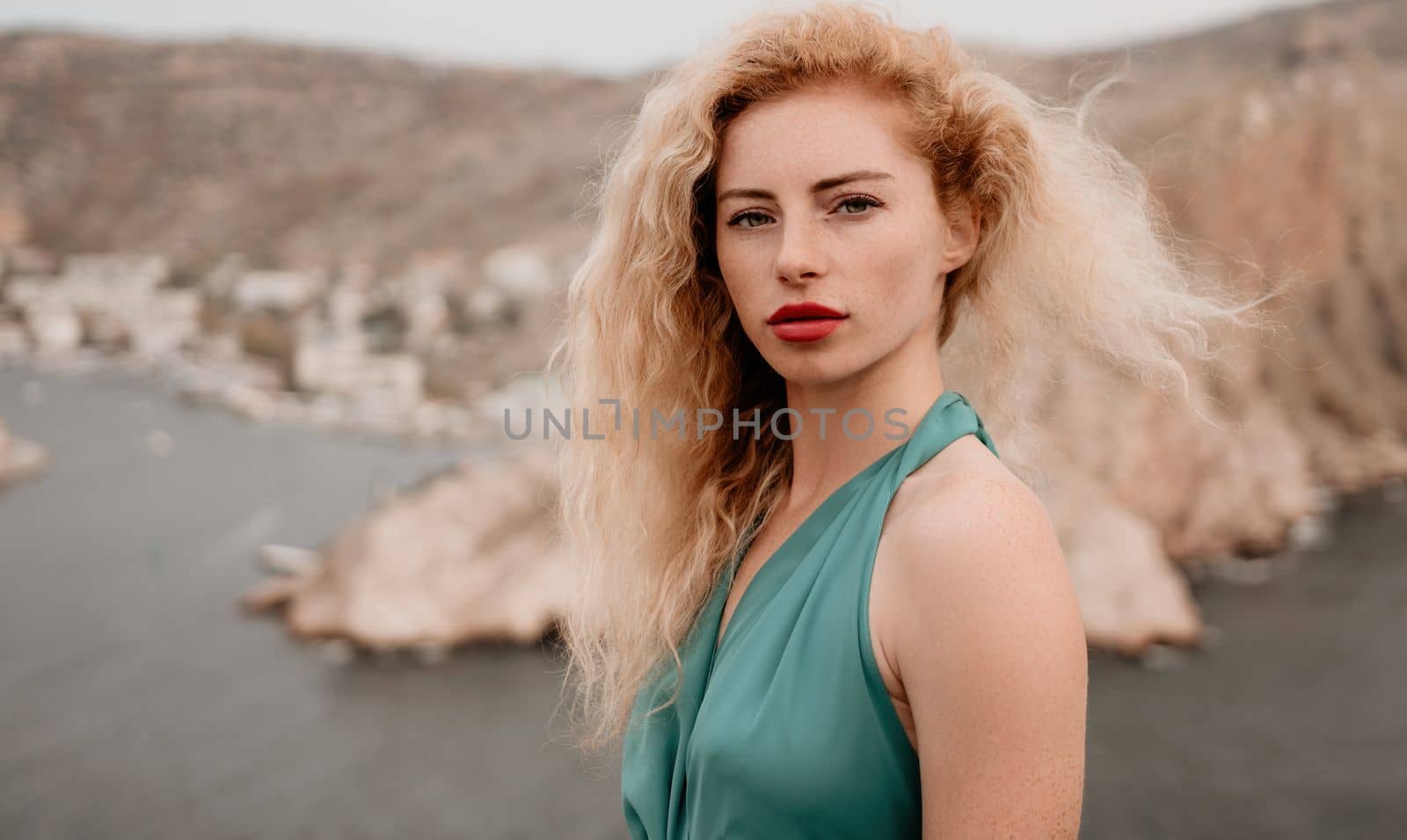 Side view a Young beautiful sensual woman in a mint long dress posing on a volcanic rock high above the sea during sunset. Girl on the nature on overcast sky background. Fashion photo