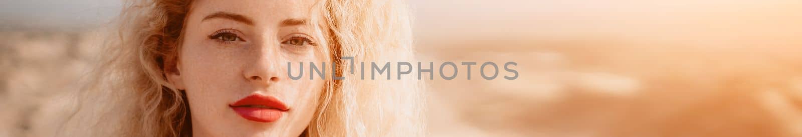 Side view a Young beautiful sensual woman in a red long dress posing on a volcanic rock high above the sea during sunset. Girl on the nature on overcast sky background. Fashion photo