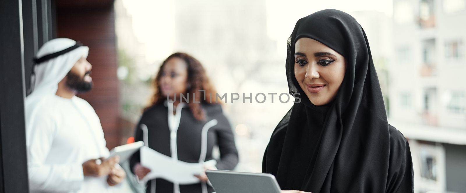 Shes got everything she needs on her tablet. an attractive young businesswoman dressed in Islamic traditional clothing using a tablet on her office balcony