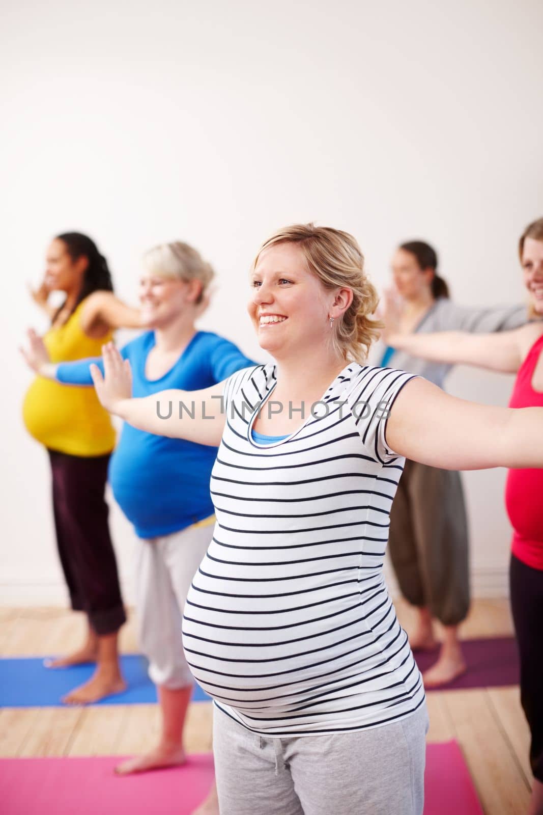 Preparing our bodies for the challenges of motherhood. A multi-ethnic group of pregnant women doing exercises with their arms stretched to the side. by YuriArcurs