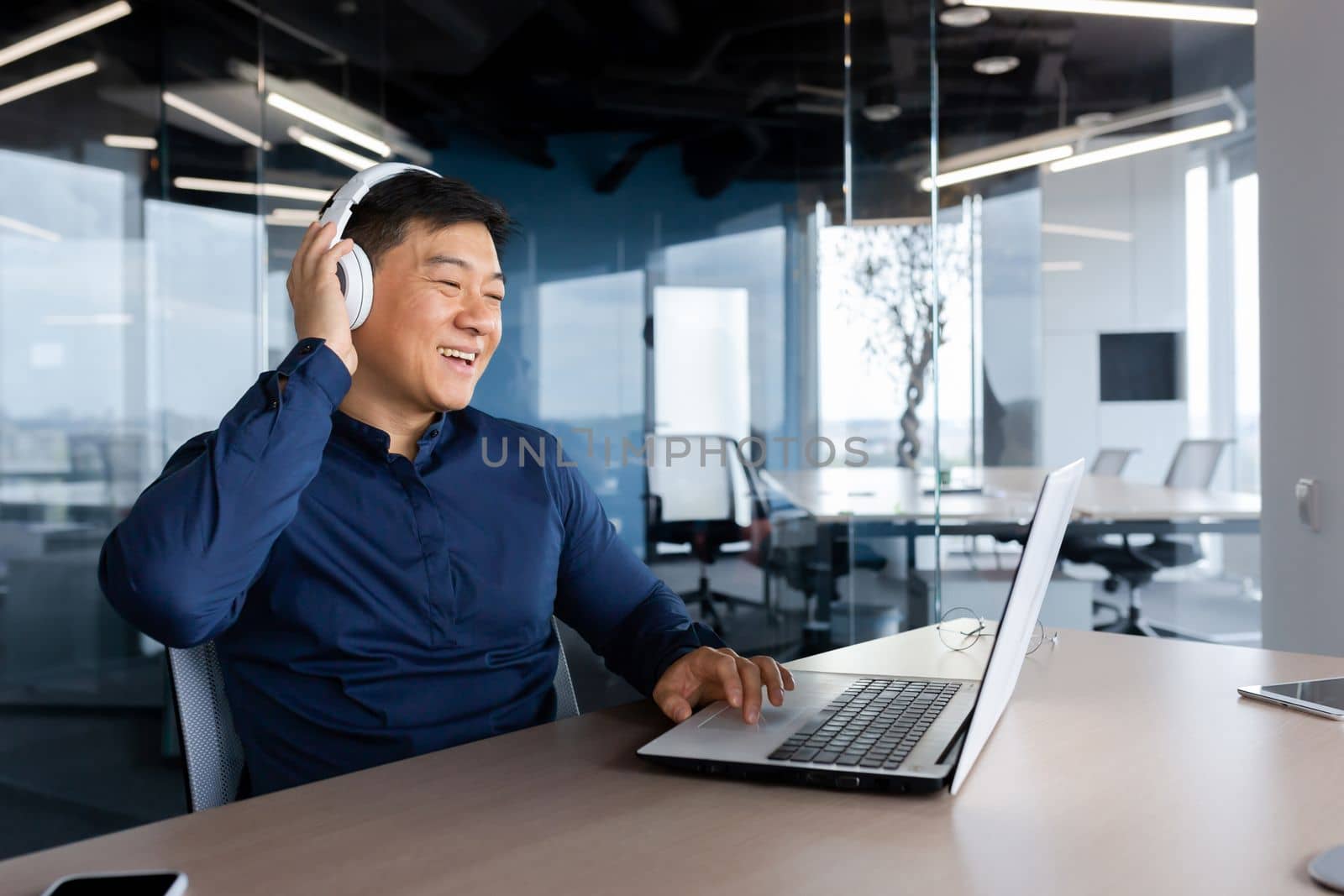 Happy young male student, freelancer, blogger listening to music in headphones. He sits in the office at a table with a laptop. Break. rests.