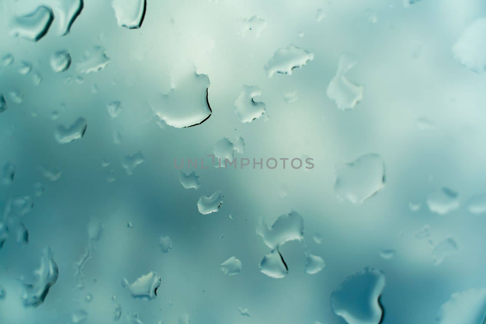 Water drops on glass against blue sky, rainy season concept. Window view background screensaver.