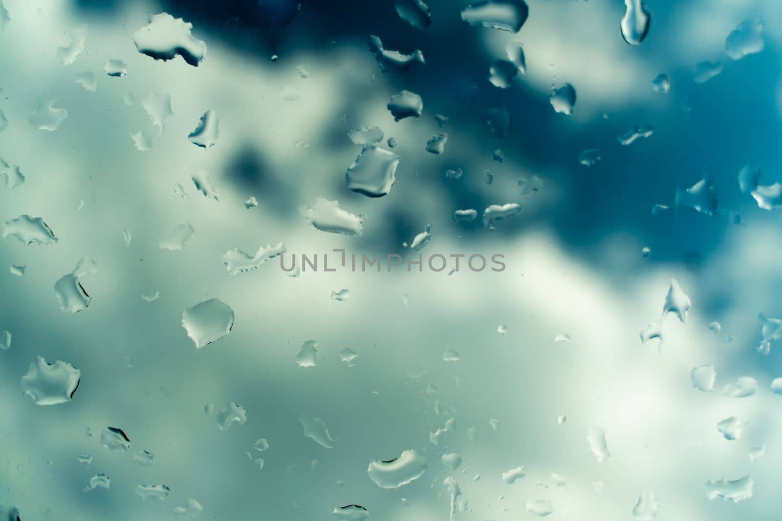 Water drops on glass against blue sky, rainy season concept. Window view background screensaver by Matiunina