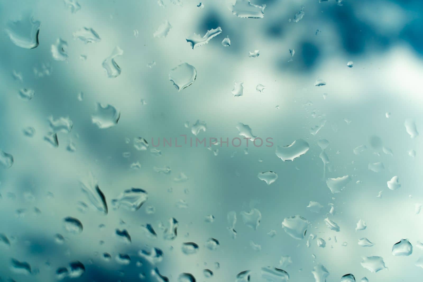 Water drops on glass against blue sky, rainy season concept. Window view background screensaver by Matiunina