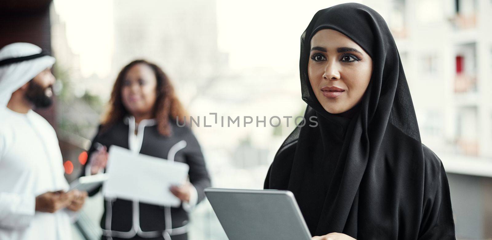 Taking her work mobile. an attractive young businesswoman dressed in Islamic traditional clothing using a tablet on her office balcony