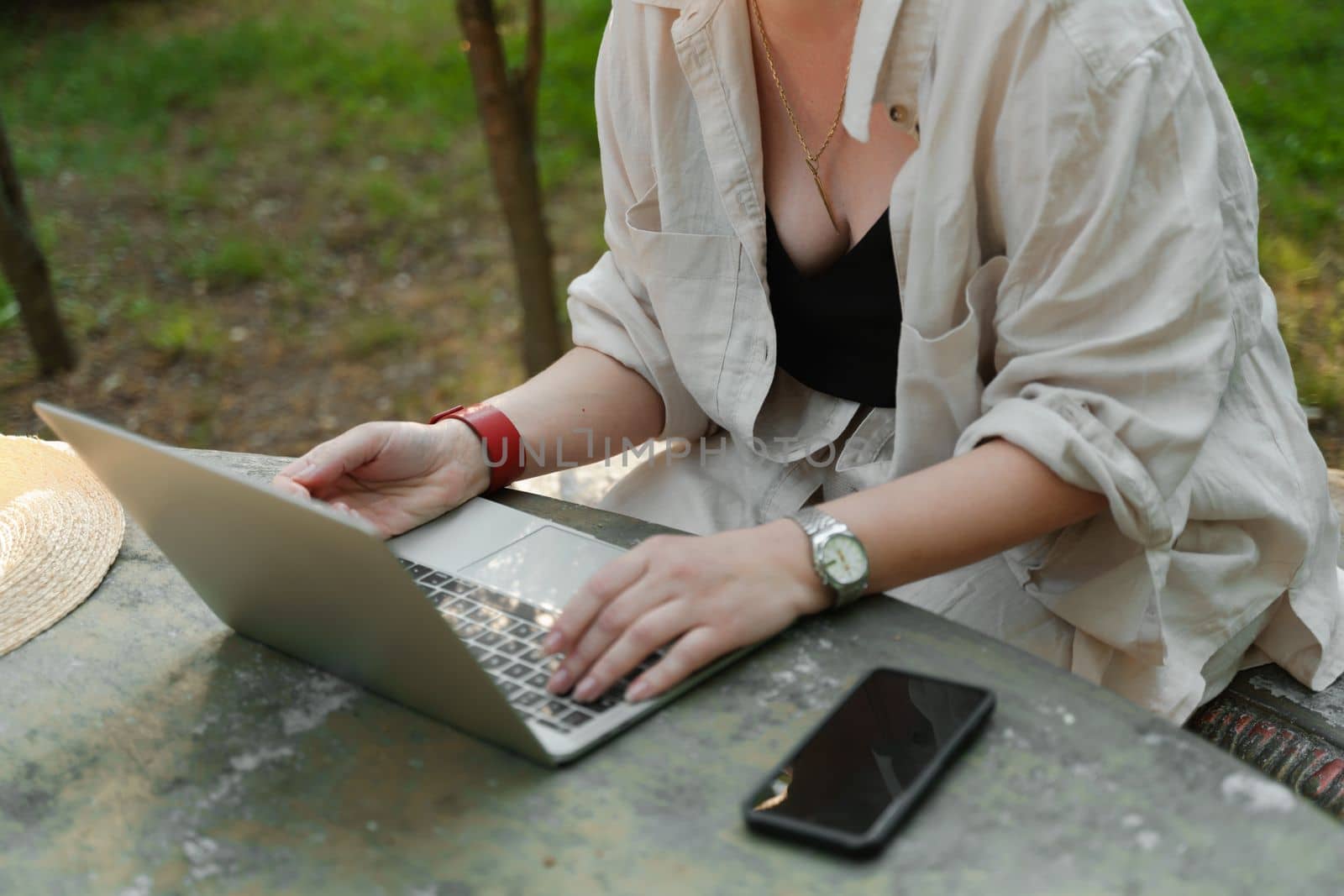 a beautiful mature woman in hat works on a computer at a white table in nature and spends her day productively.